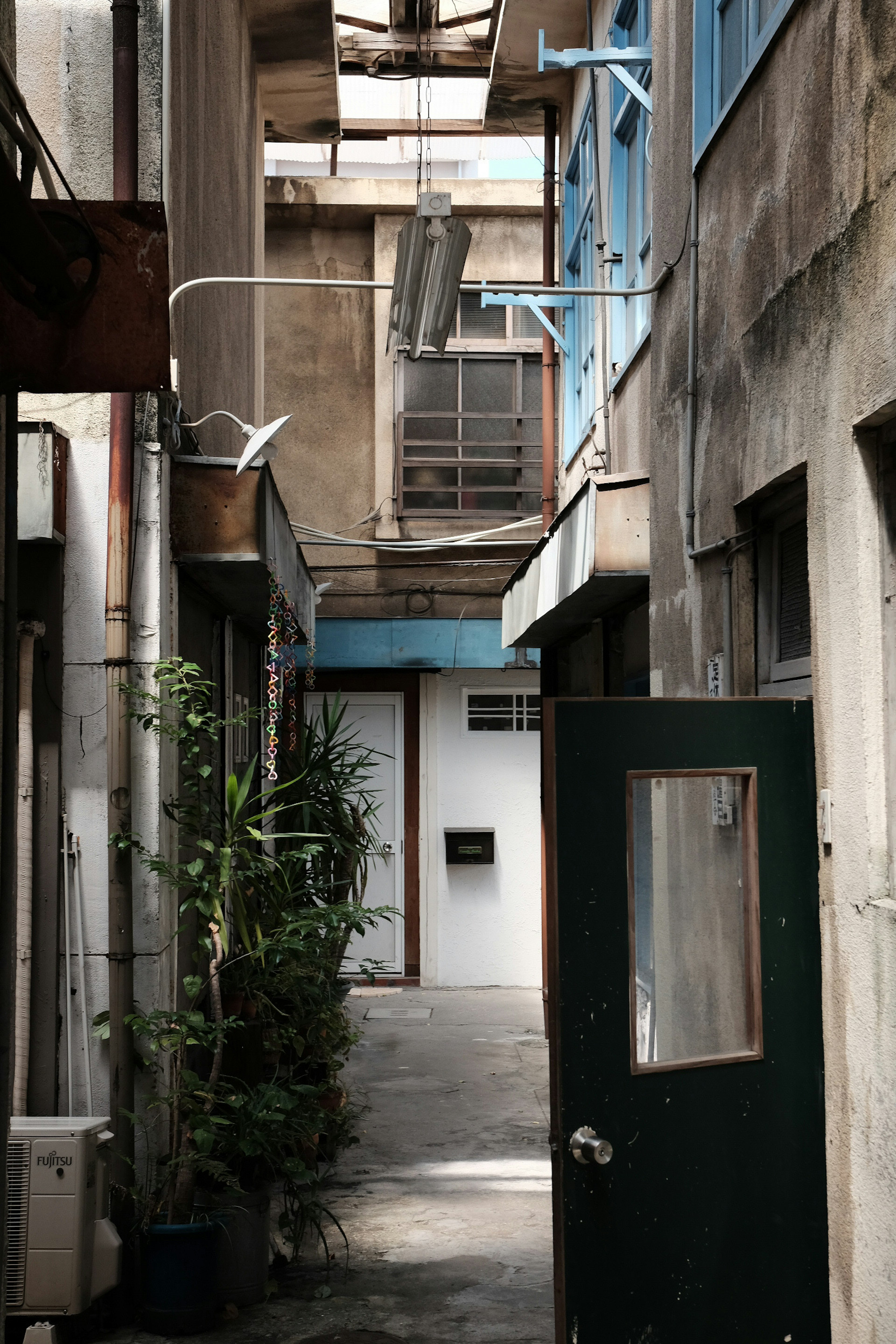 Callejón estrecho con paredes desgastadas y ventanas azules Puerta verde y plantas visibles