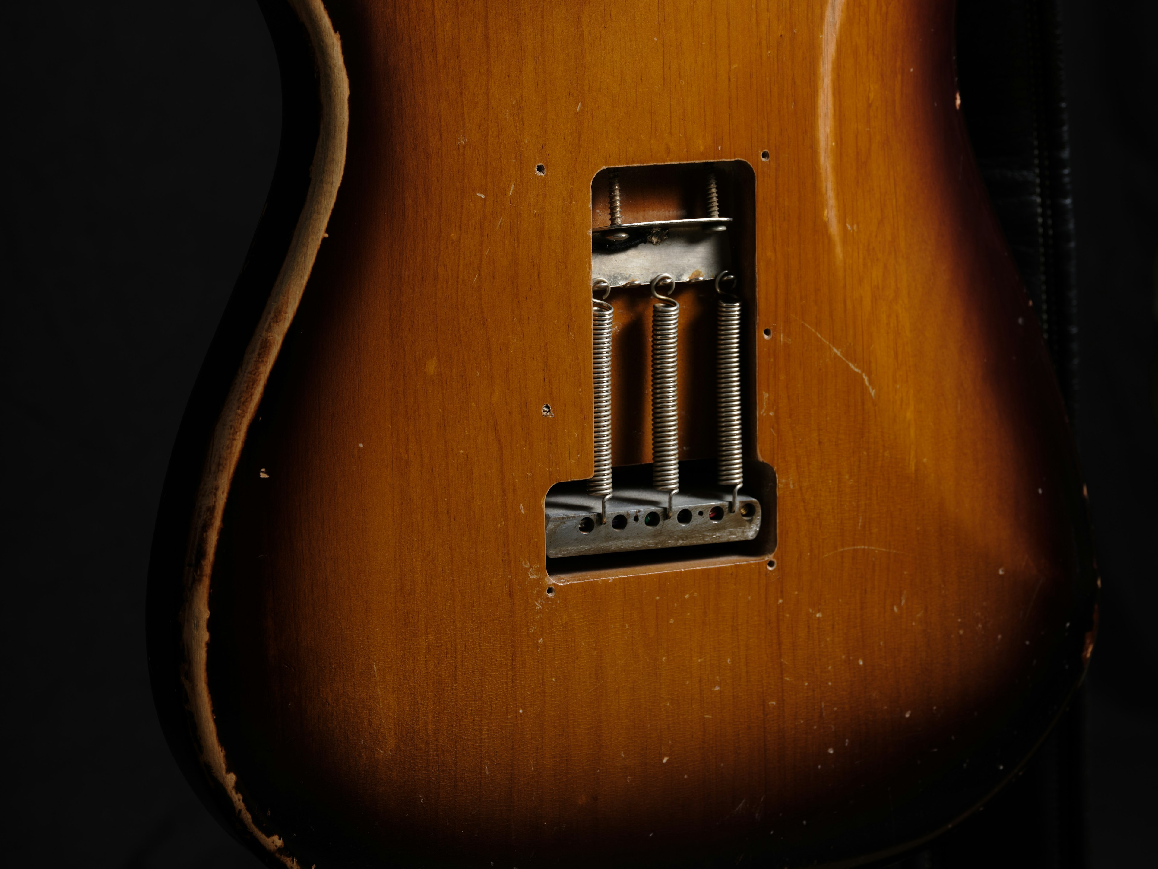 Close-up image of a guitar body showing warm brown tones and visible metal parts