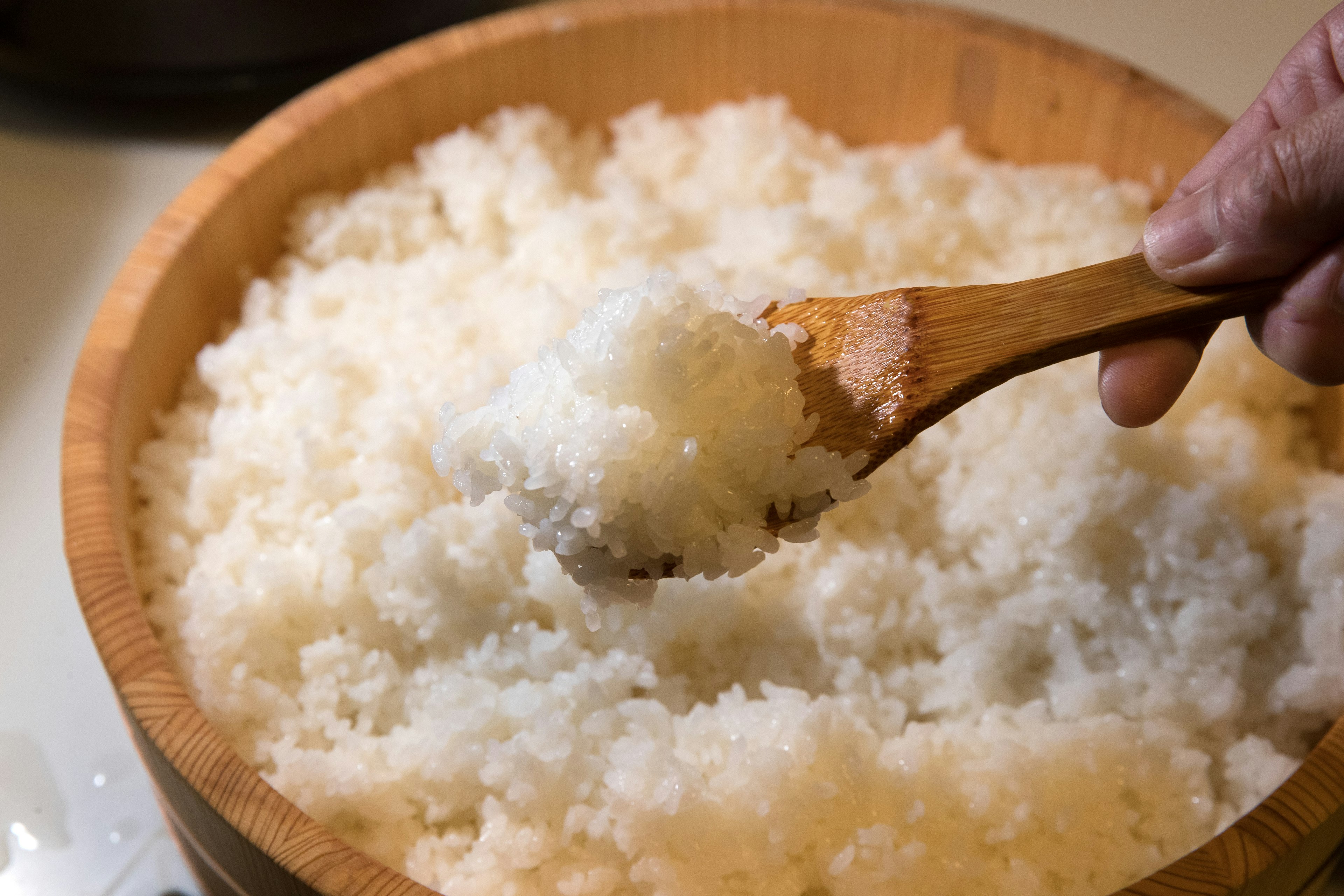 Hand scooping fluffy white rice with a wooden spoon