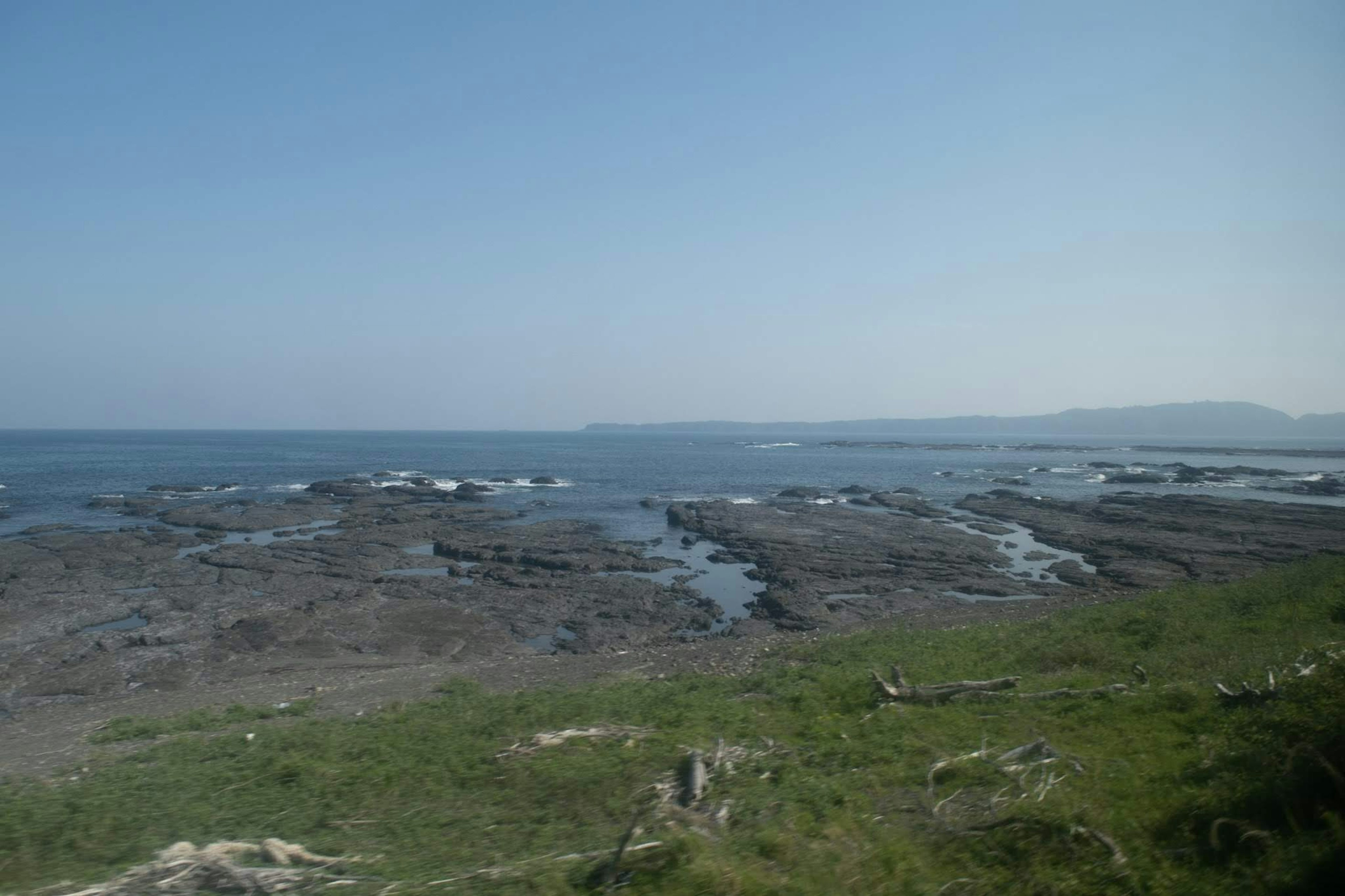 Pemandangan laut dengan pantai berbatu dan rumput hijau di bawah langit biru jernih