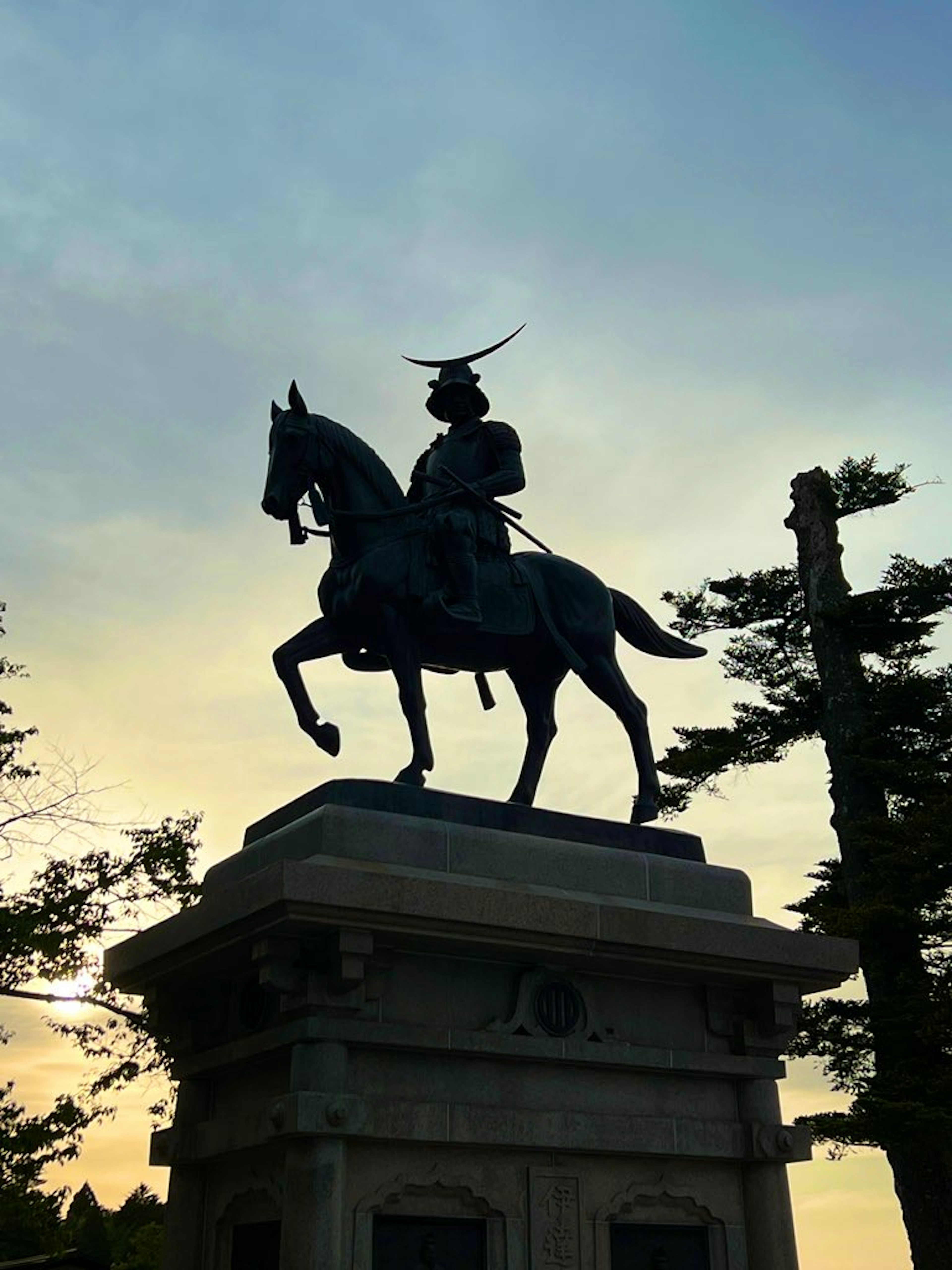 Silhouette of a samurai statue on horseback against a sunset sky