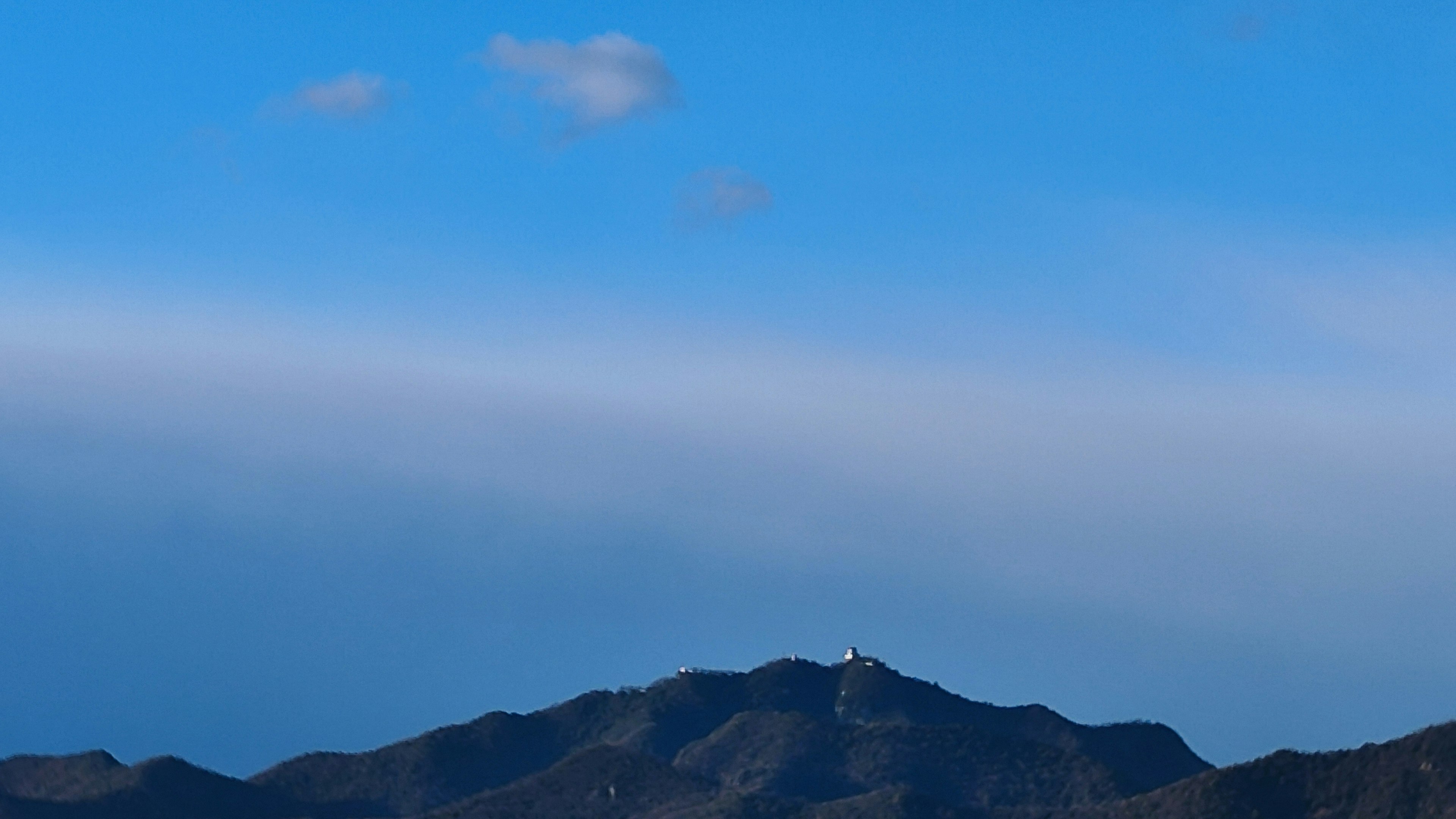 Montañas bajo un cielo azul con un pequeño edificio blanco en la cima