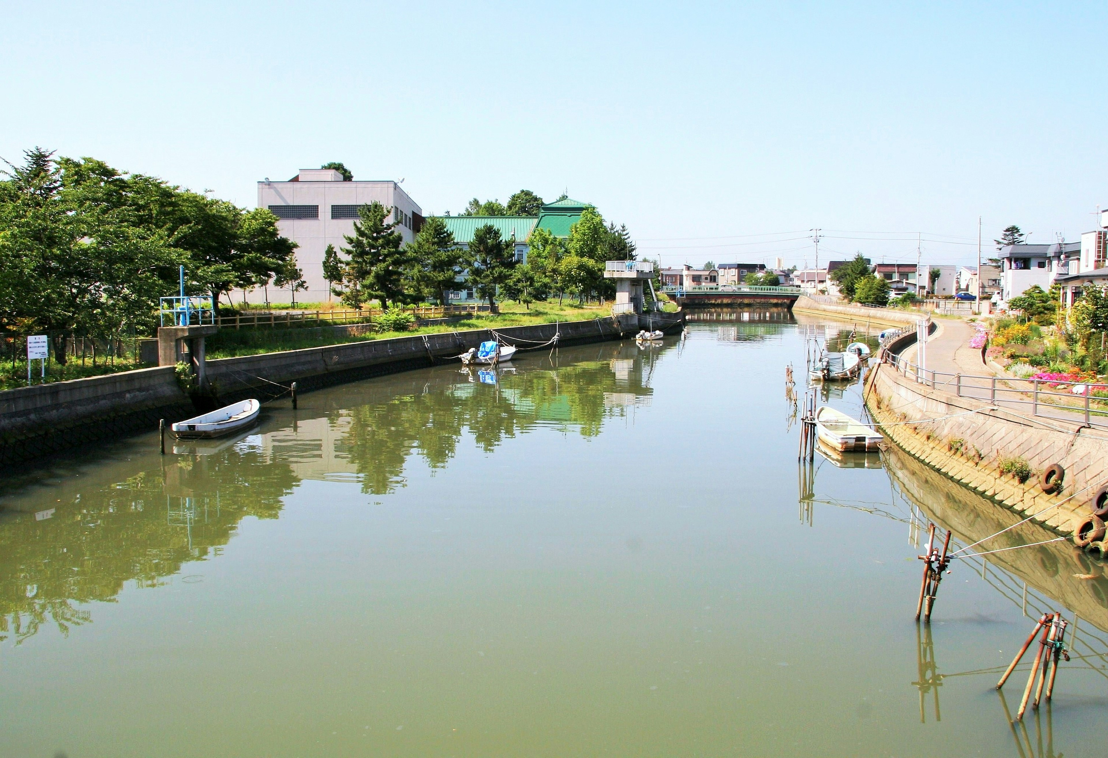 Serene river landscape with calm water boats moored along the banks lush greenery and bright sky