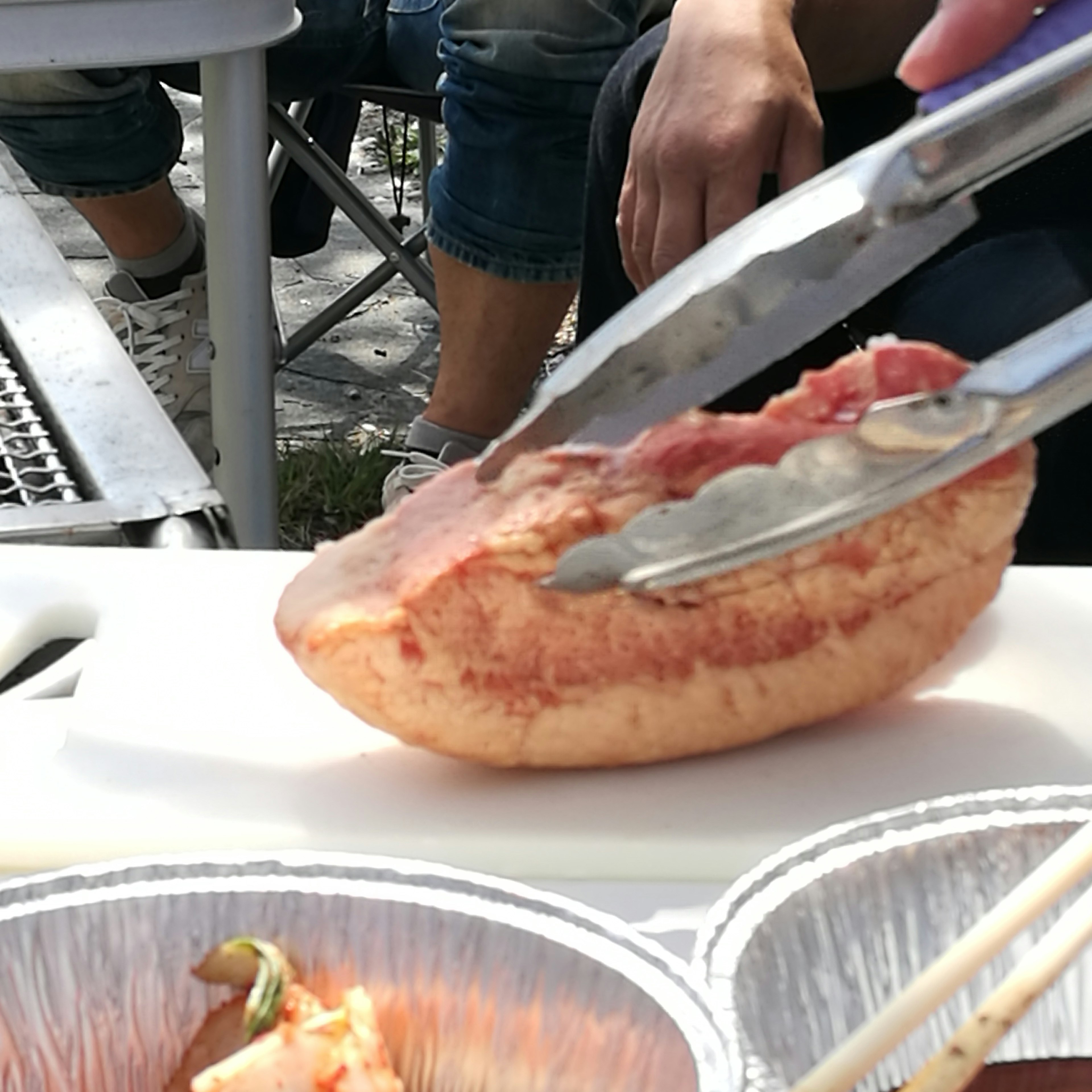 Outdoor dining scene with tongs gripping a large piece of meat