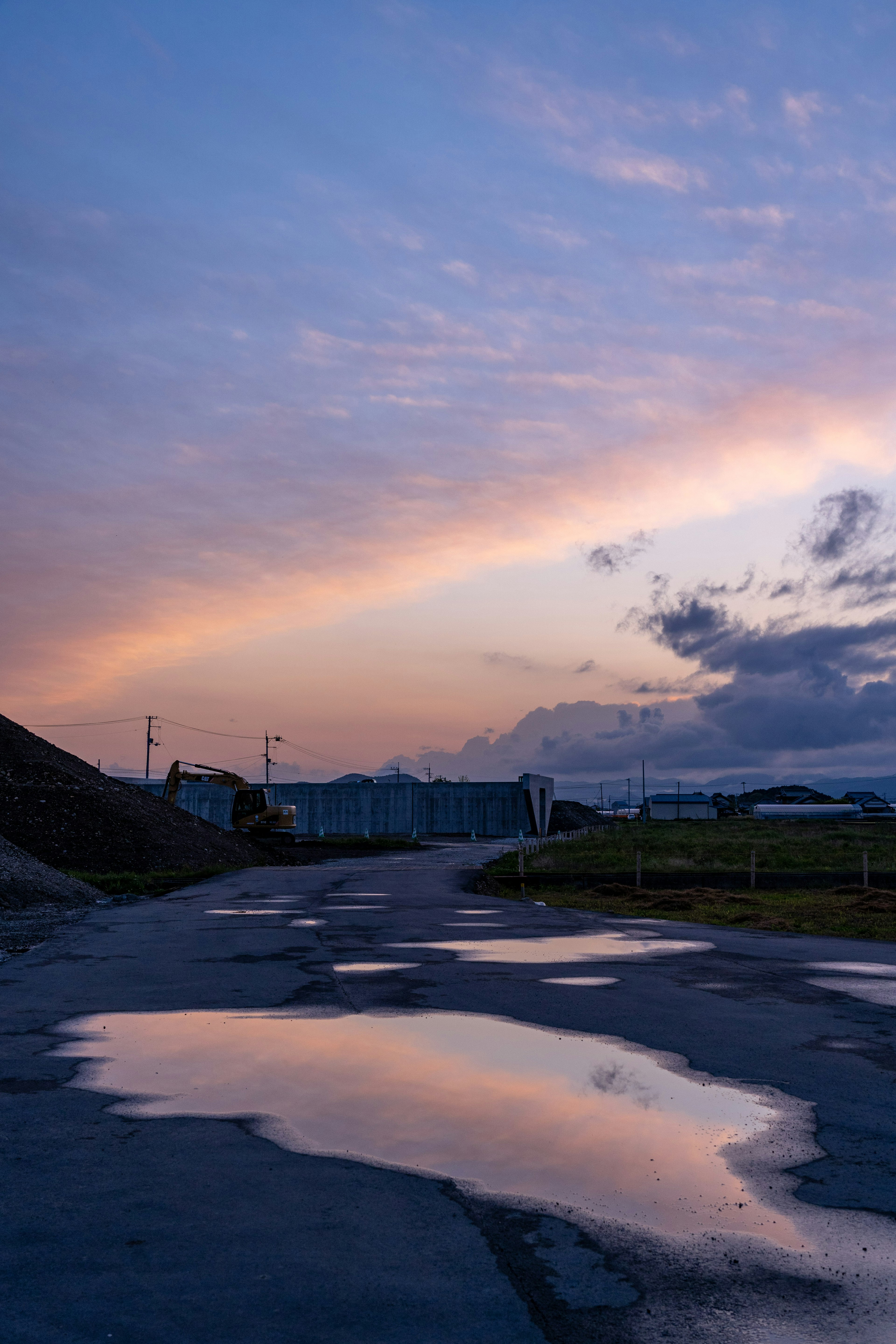 Eine Straße, die einen Sonnenuntergangshimmel mit Wasserpfützen reflektiert