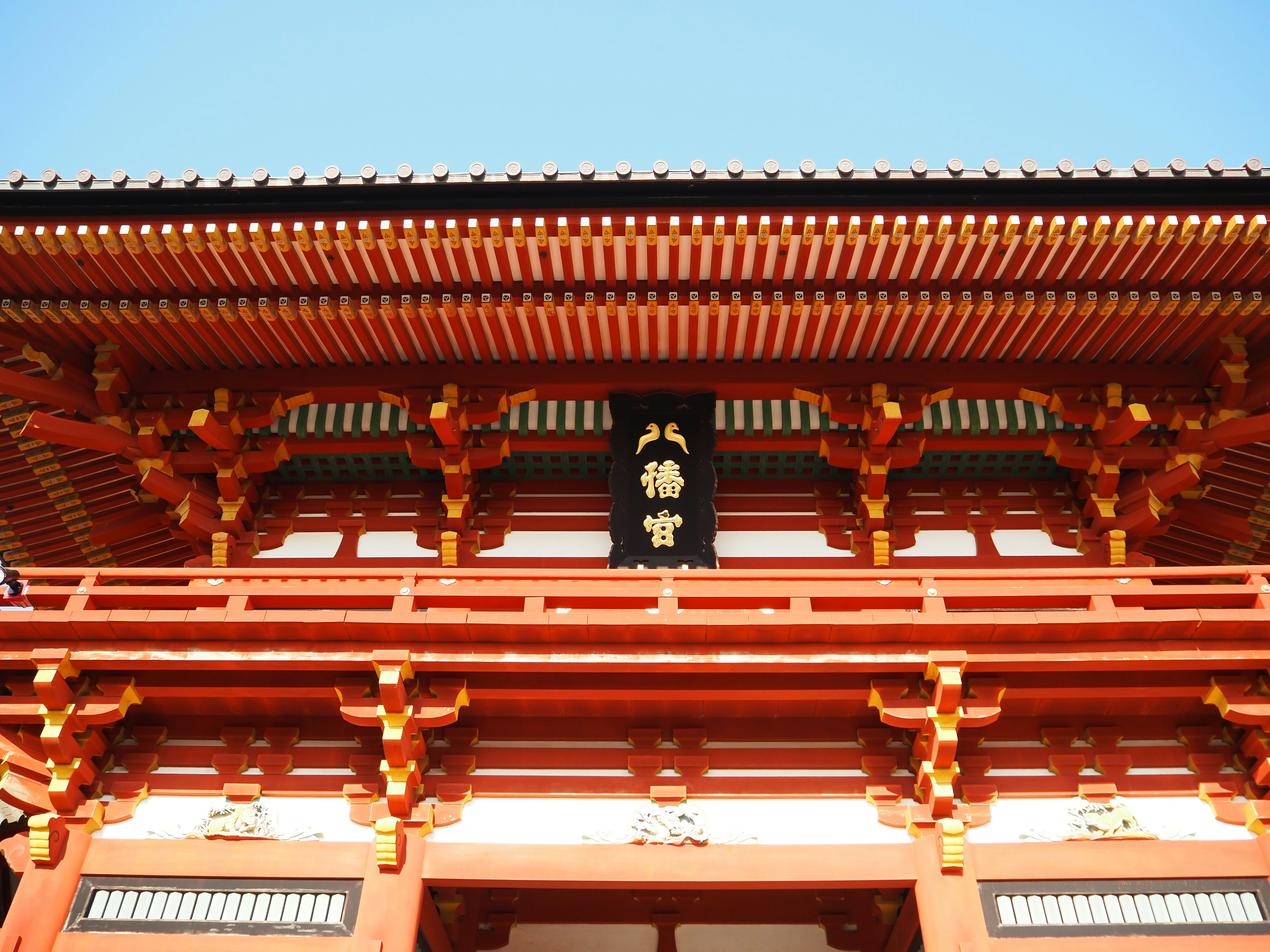 Eksterior kuil Jepang tradisional dengan struktur kayu merah dan detail ornamen di bawah langit biru