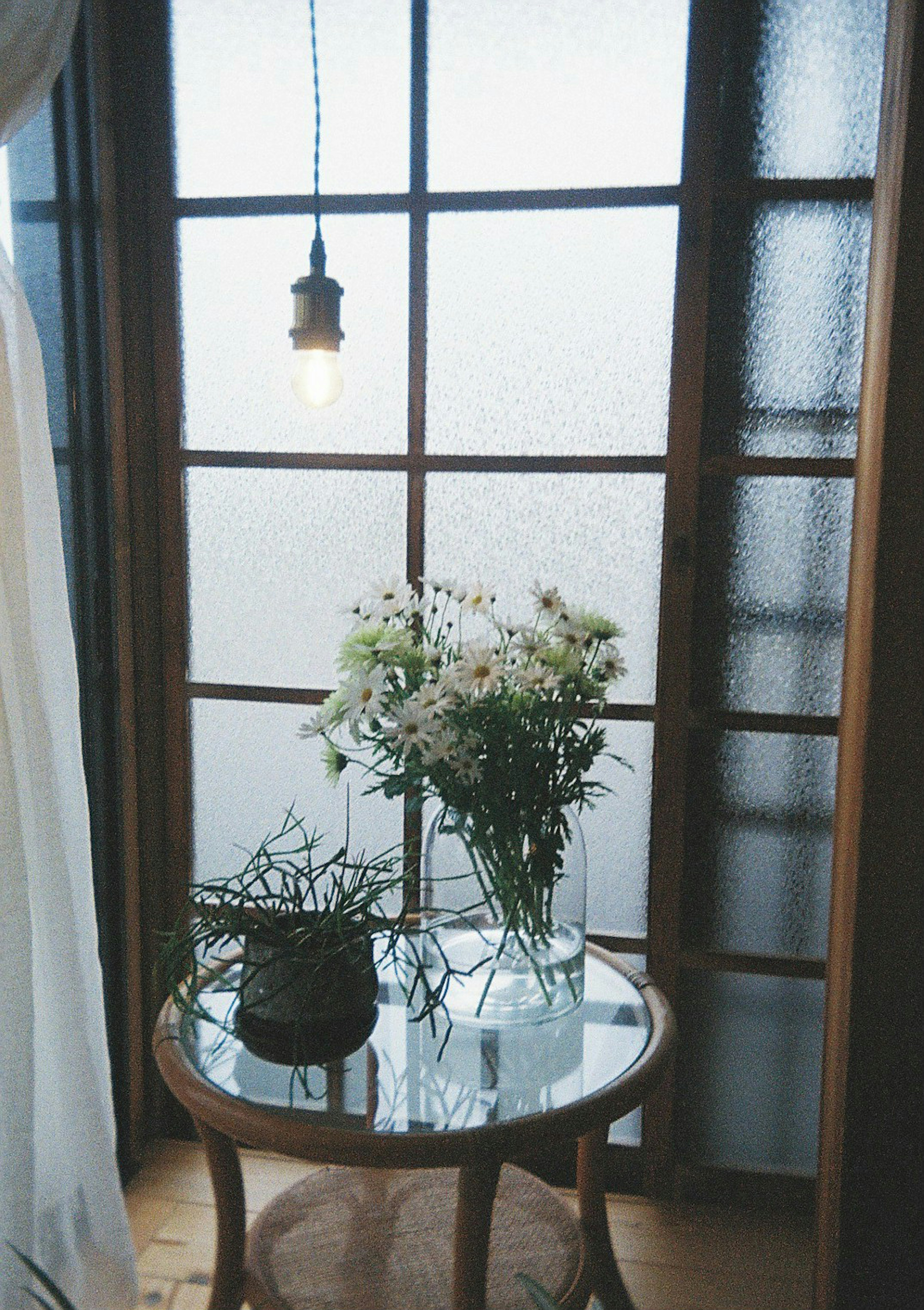 Mesa con un jarrón de flores y una planta cerca de una ventana