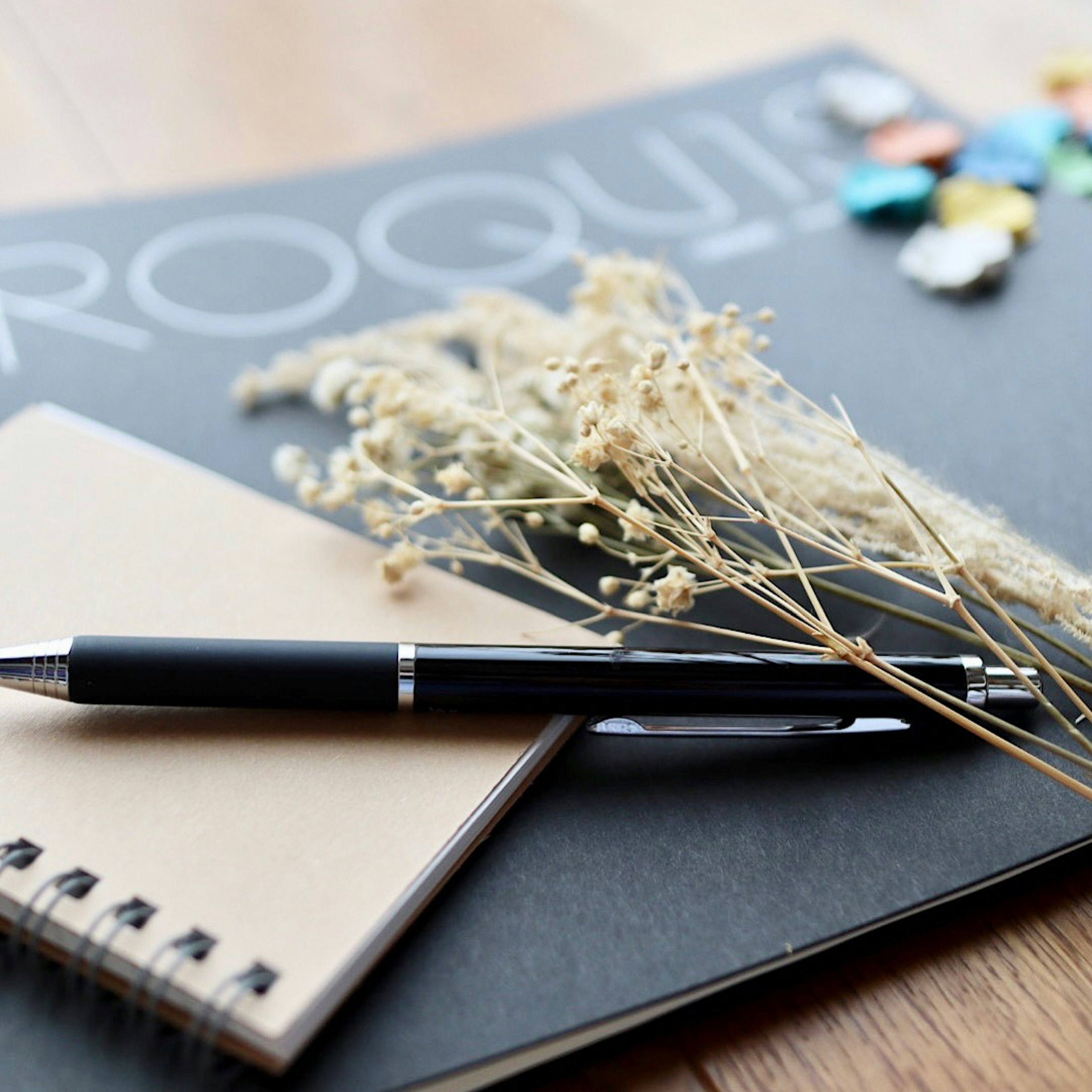 A serene desk scene featuring a black notebook and a small notepad with a pen