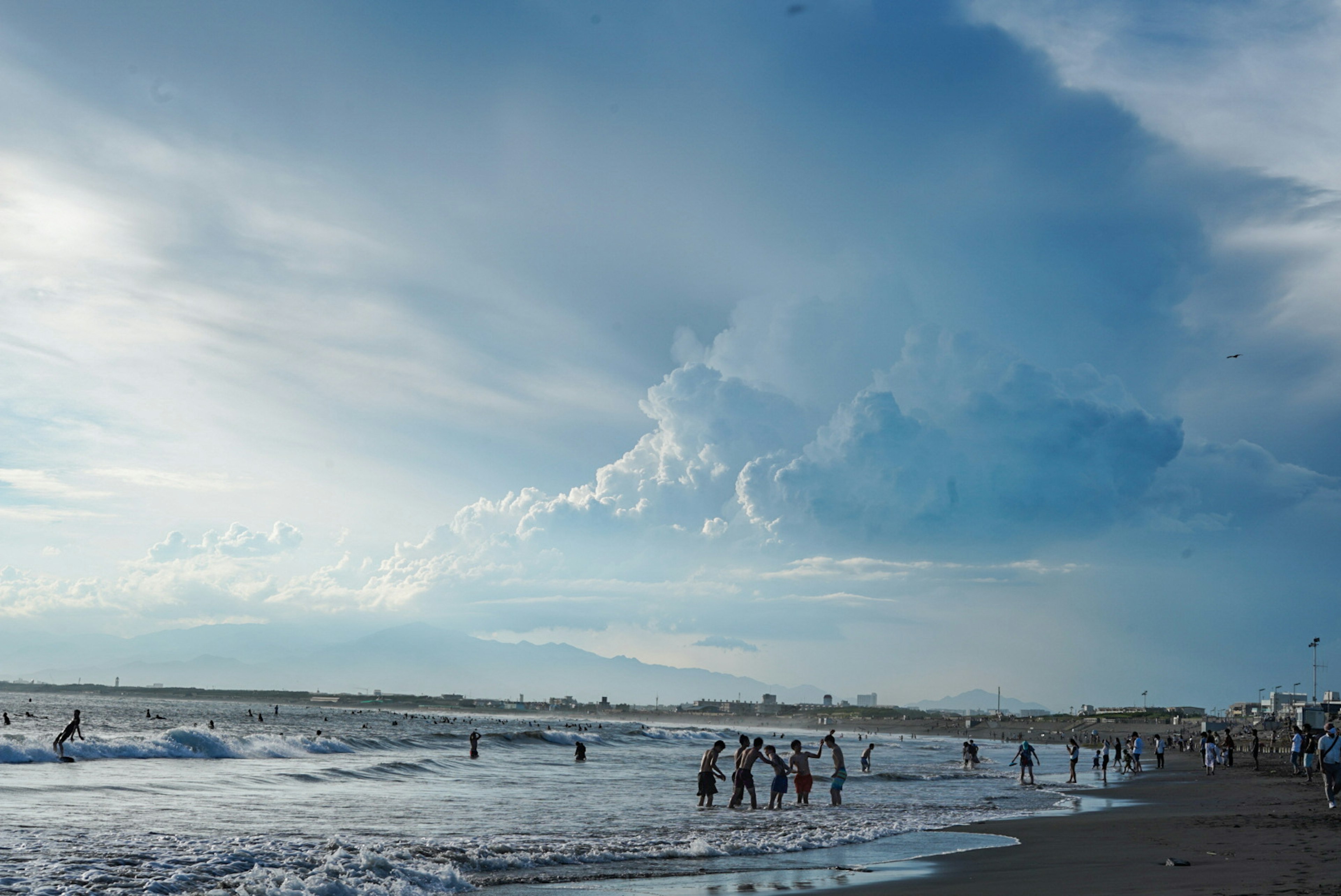 青い空と雲の下で海で遊ぶ人々のシーン