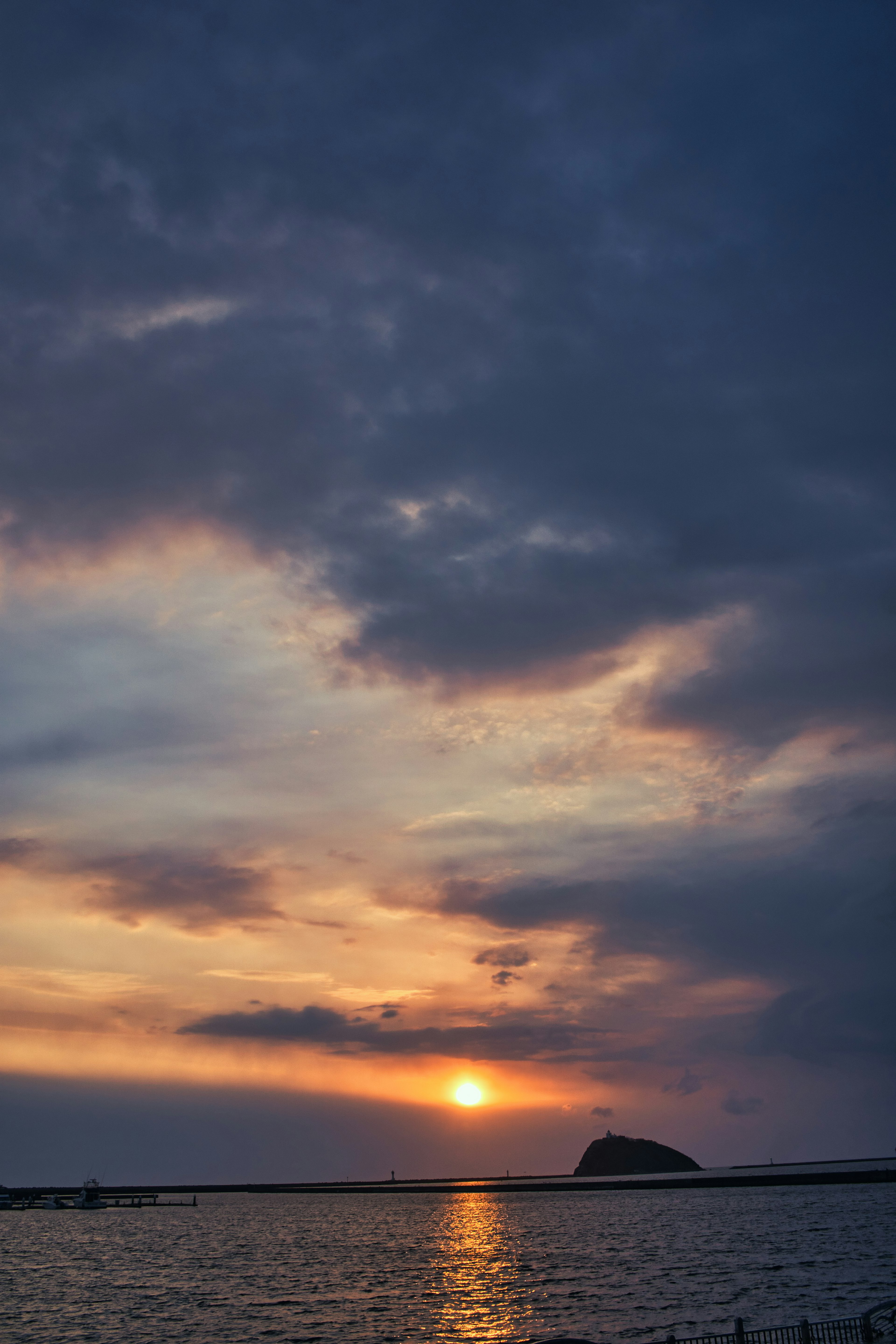 Sunset over the sea with clouds and a distant rock formation