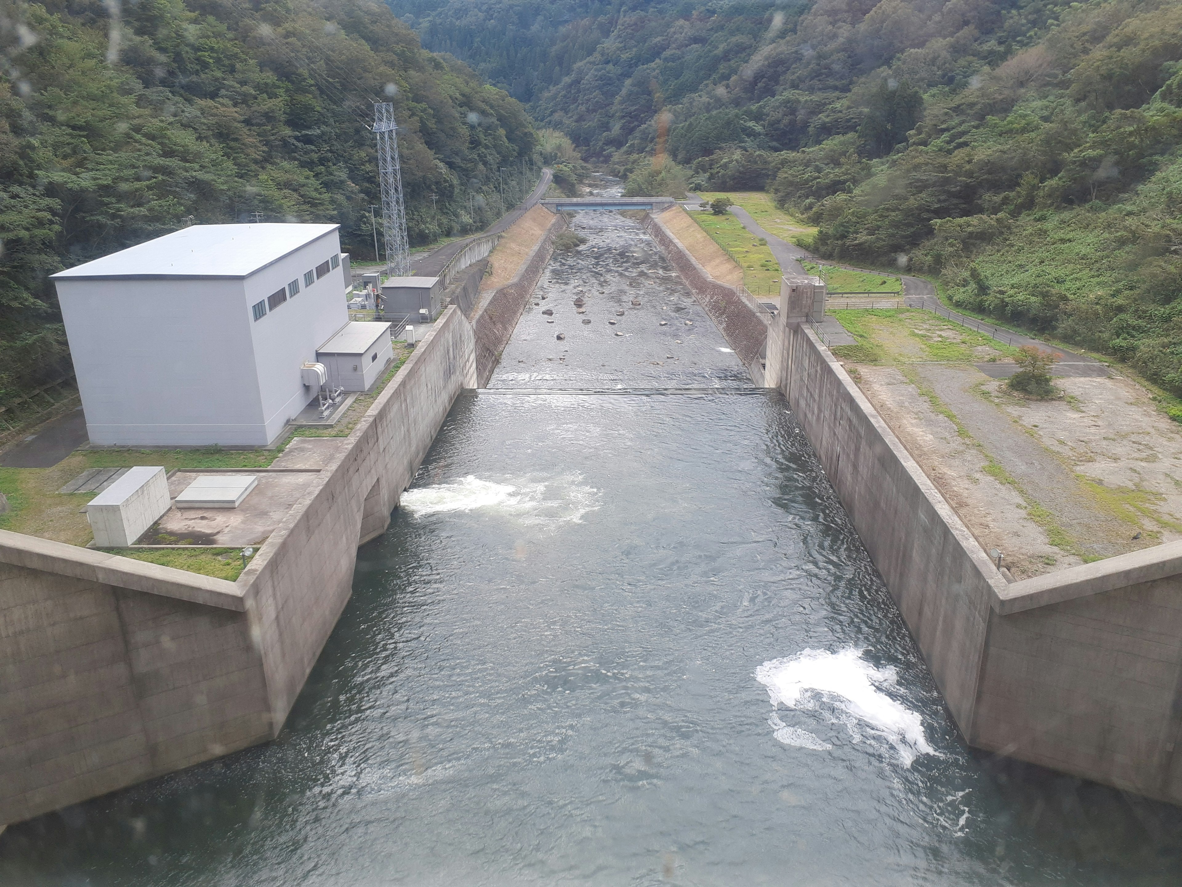 Aerial view of a dam and waterway with a nearby building and grassy area