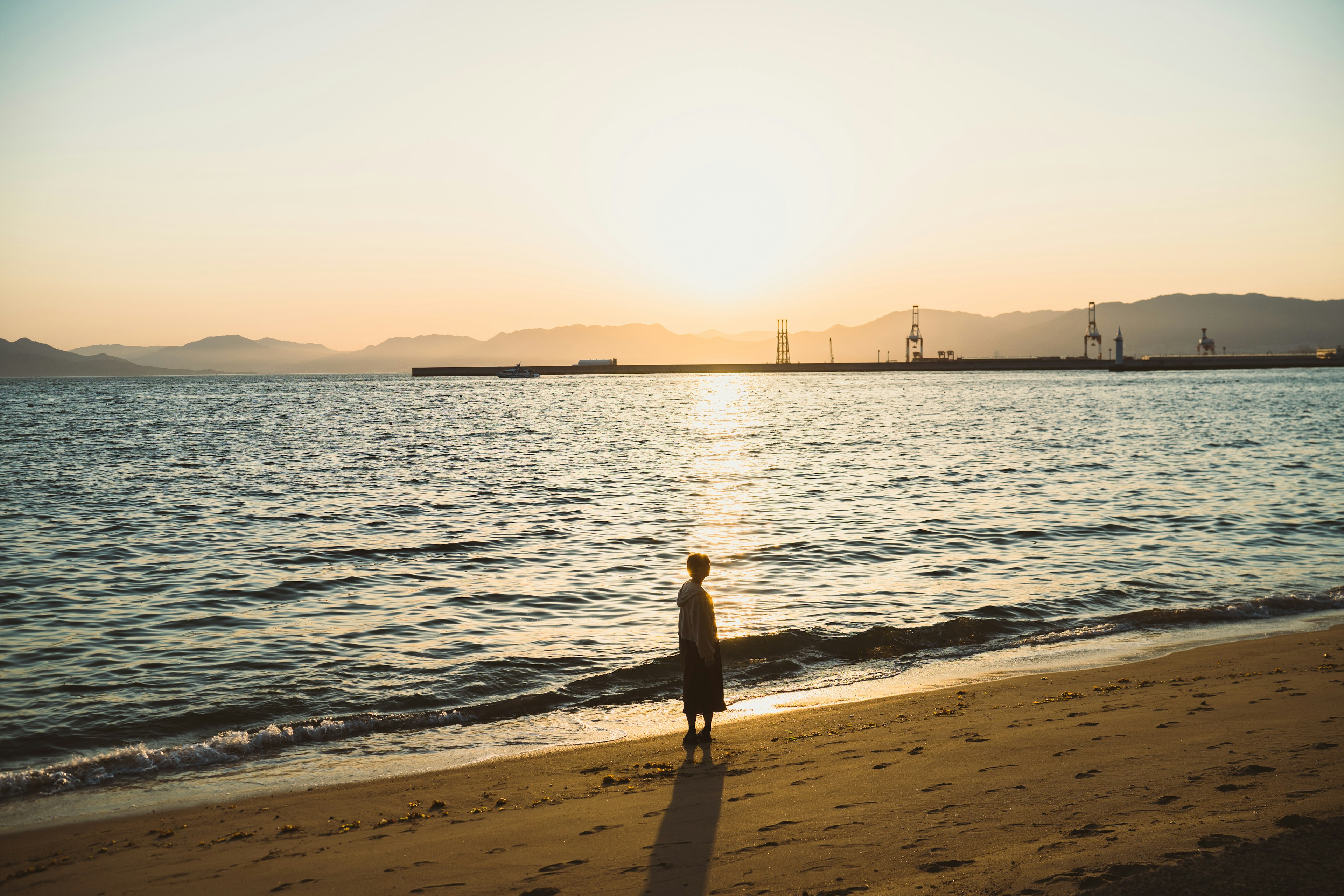 Silhouette d'une personne se tenant sur la plage au coucher du soleil