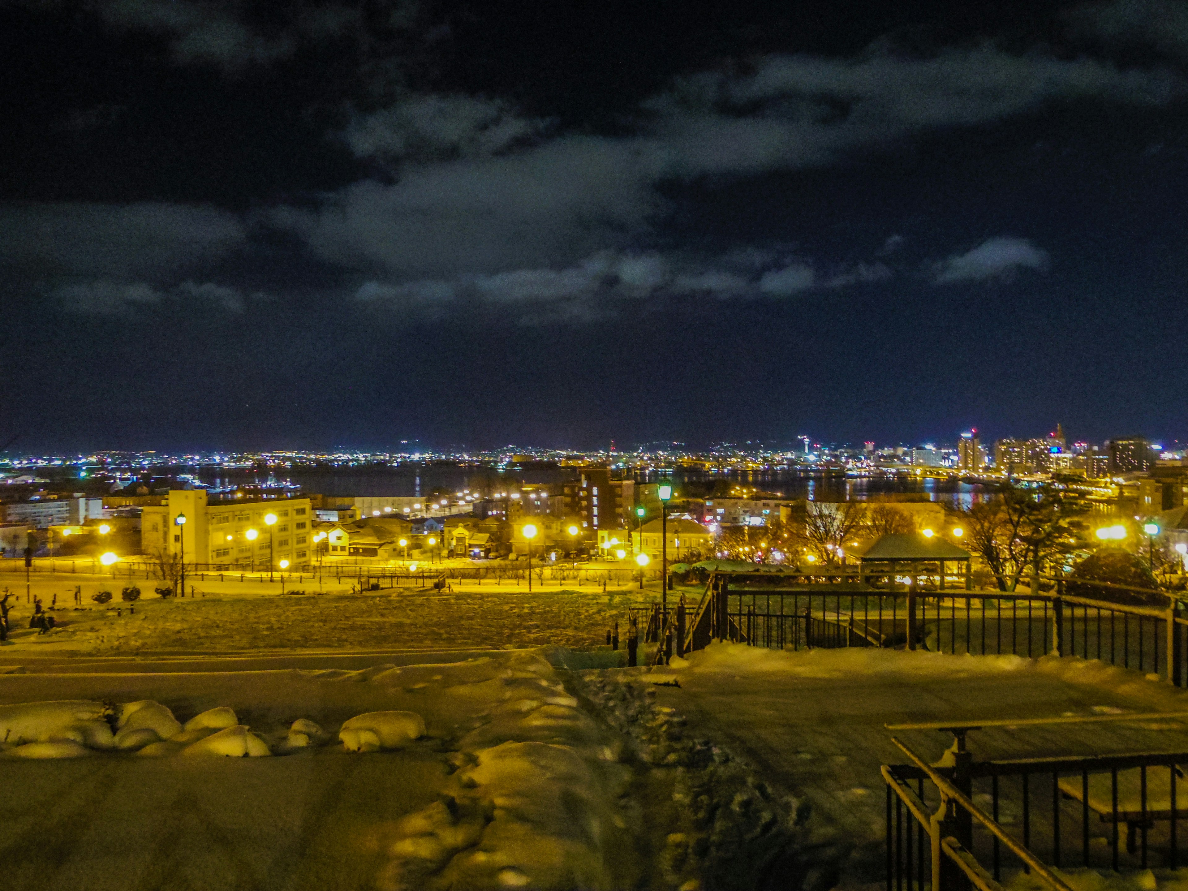 Städtische Nachtlandschaft mit beleuchteten Gebäuden vor einem Nachthimmel und schneebedecktem Vordergrund