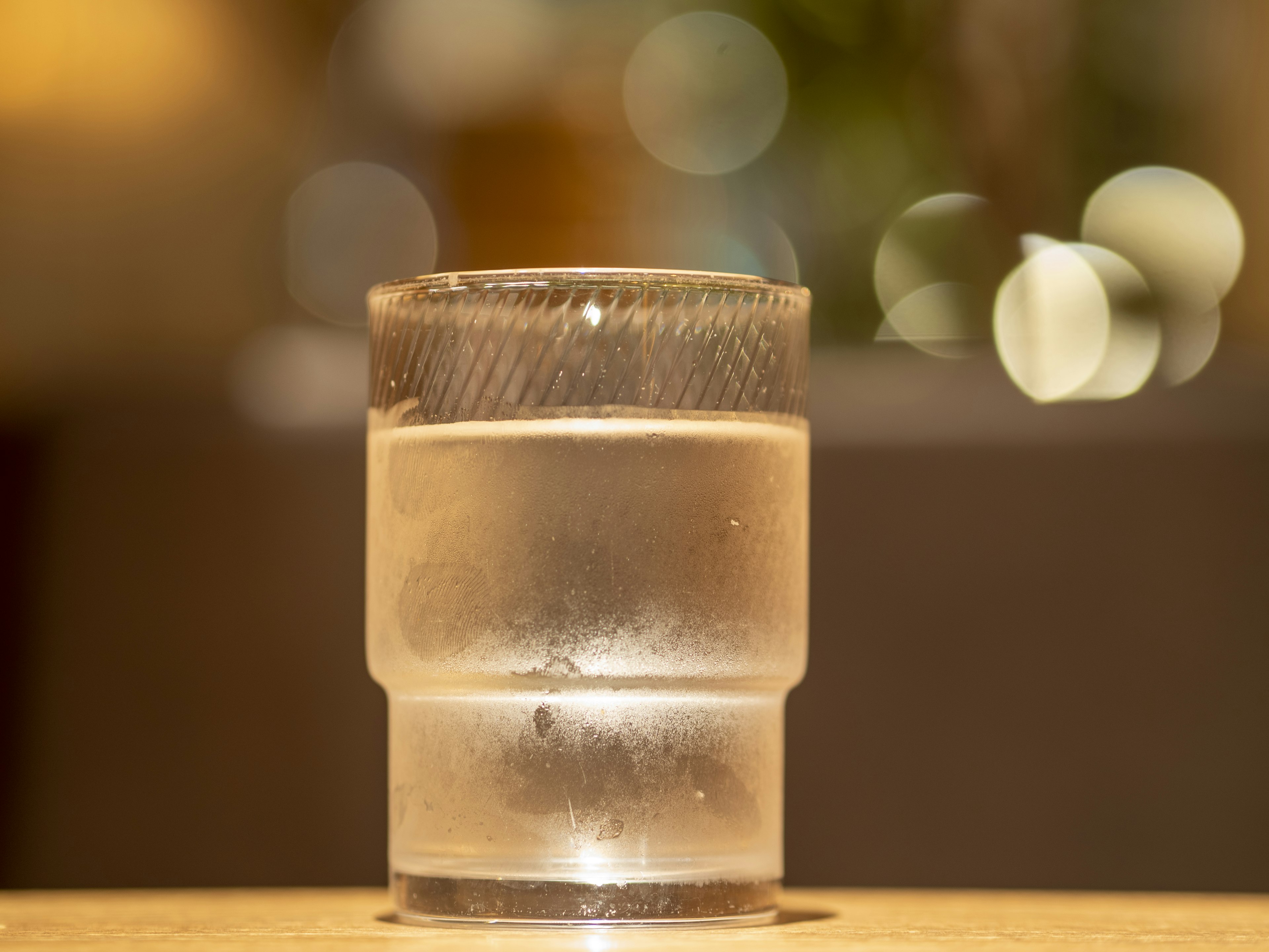 Un vaso transparente lleno de agua con un fondo borroso de luces