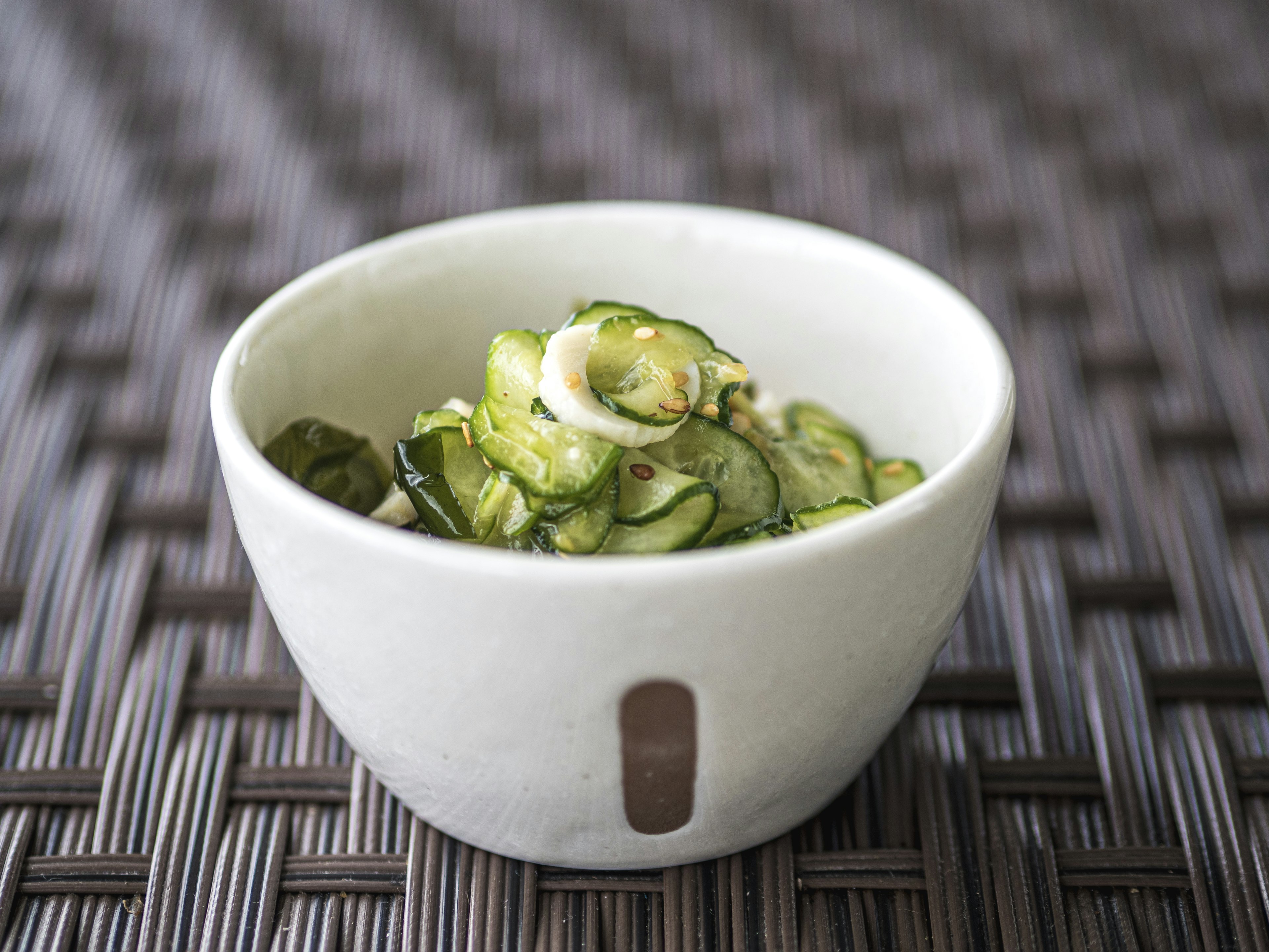 Sliced cucumber pickles in a white bowl on a textured table