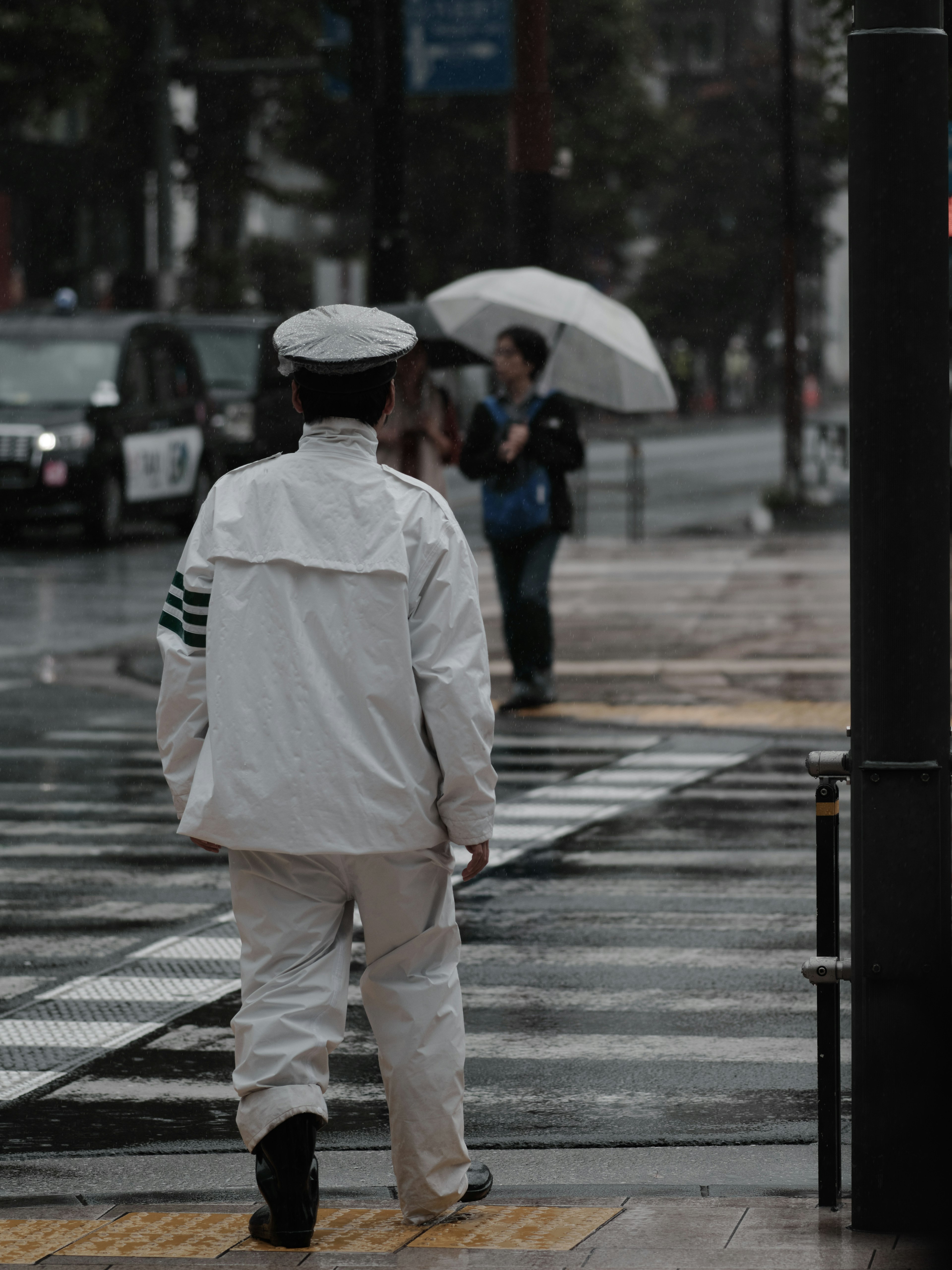 Ein Polizist in weißer Uniform, der im Regen geht, mit Menschen, die Regenschirme halten