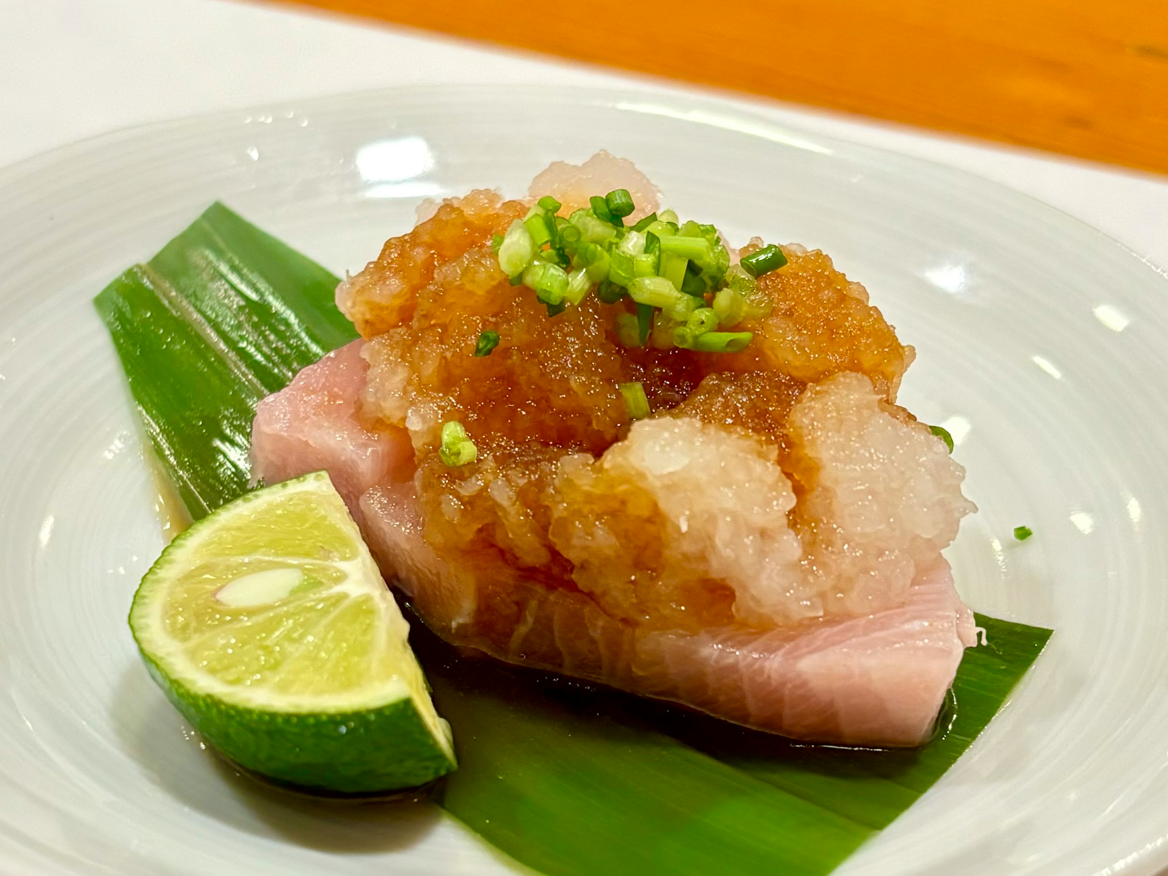 Un plat de poisson garni de radis râpé et d'oignons verts accompagné d'un quartier de lime