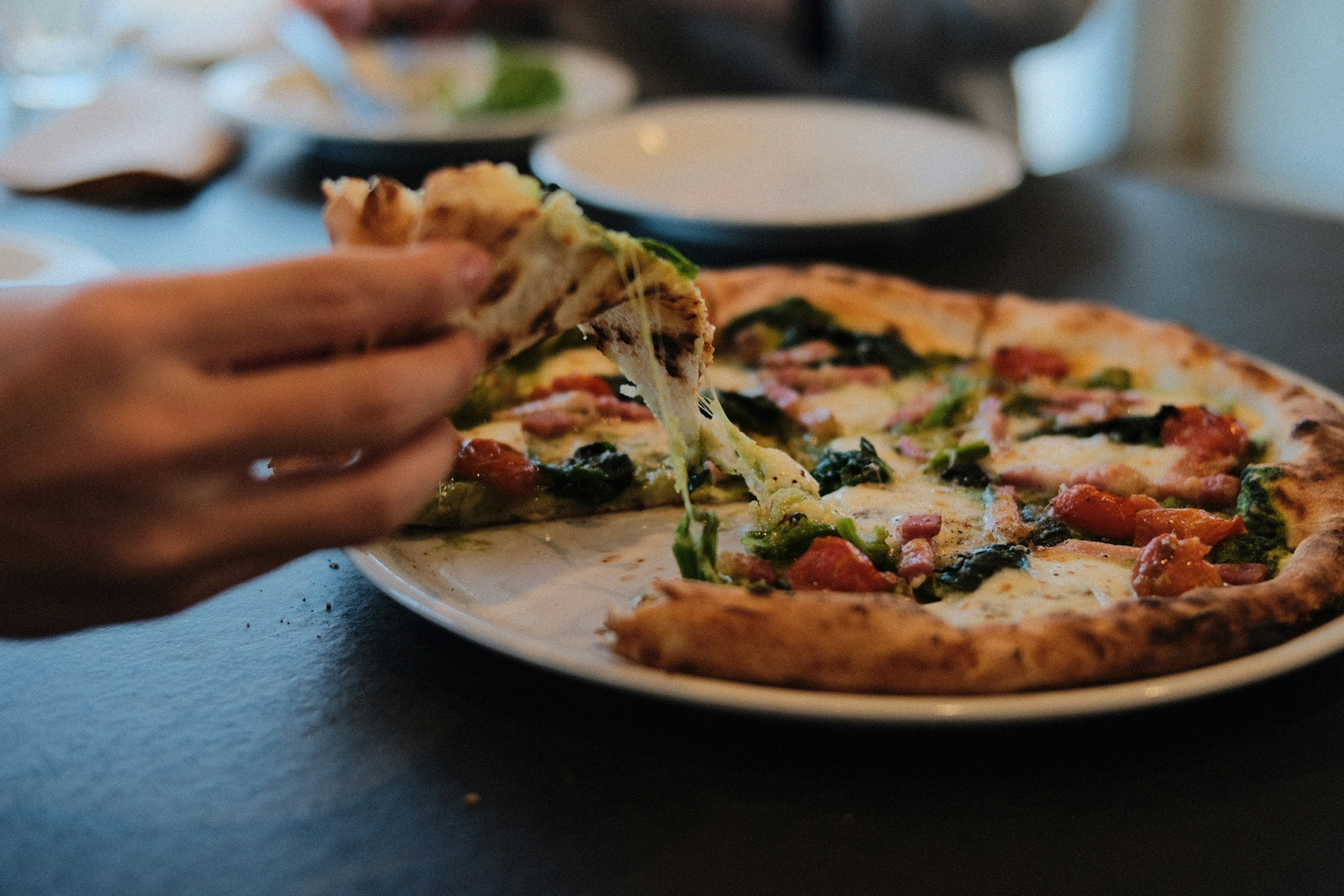 A hand lifting a slice of pizza with green vegetables on top