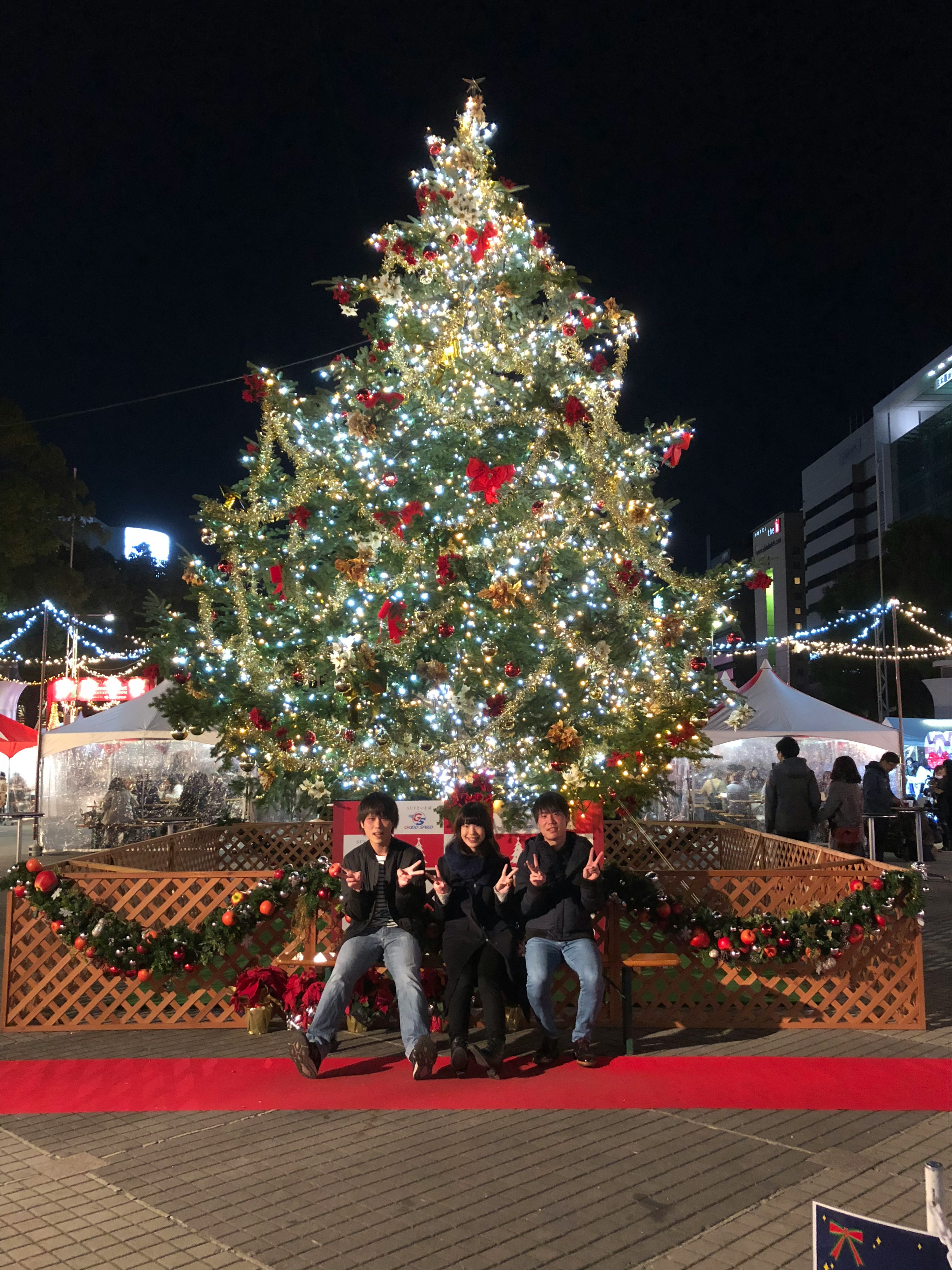 Orang-orang berpose di depan pohon Natal yang diterangi di malam hari