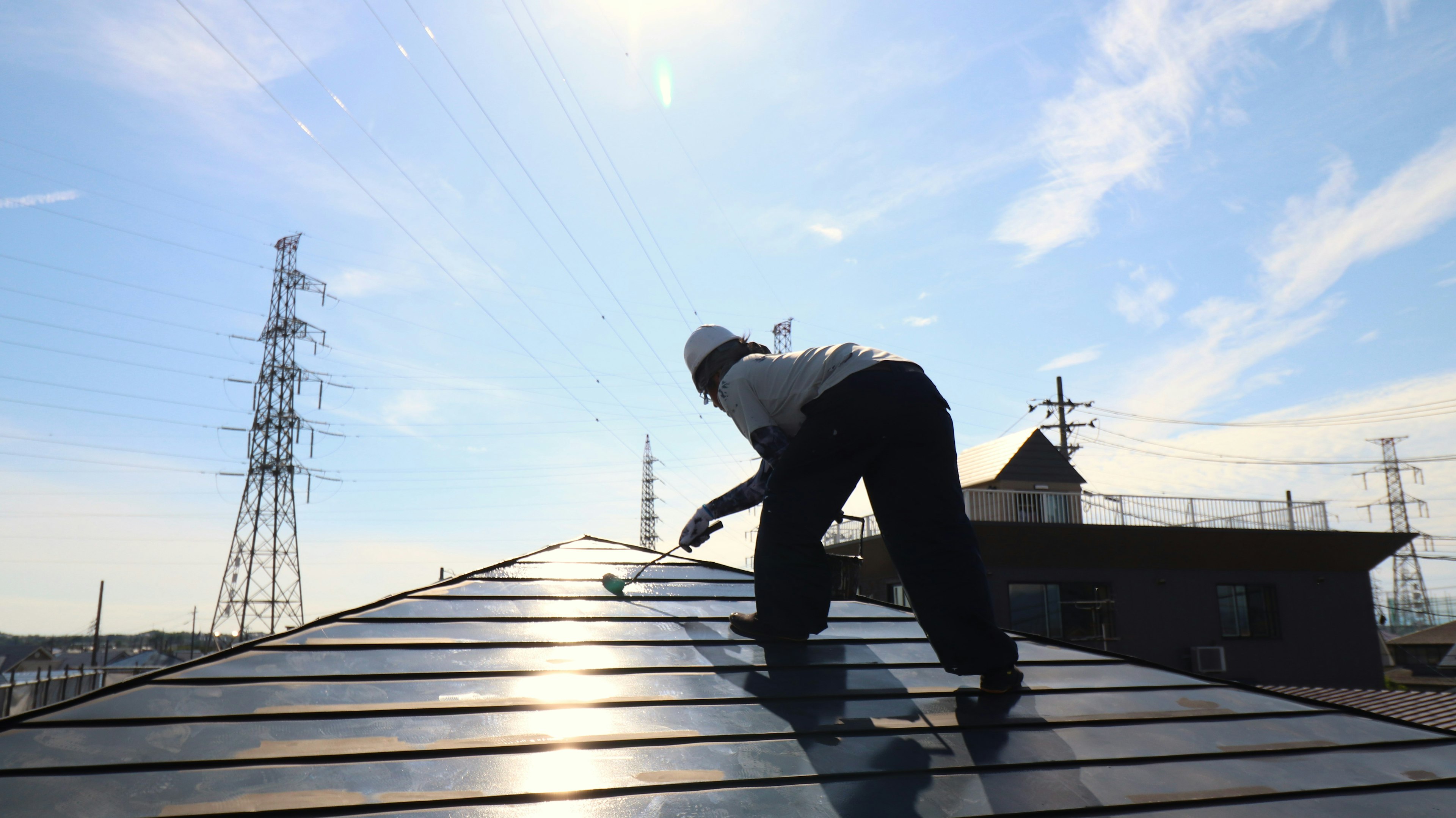 Un trabajador realizando tareas en un tejado con un cielo brillante y líneas eléctricas al fondo