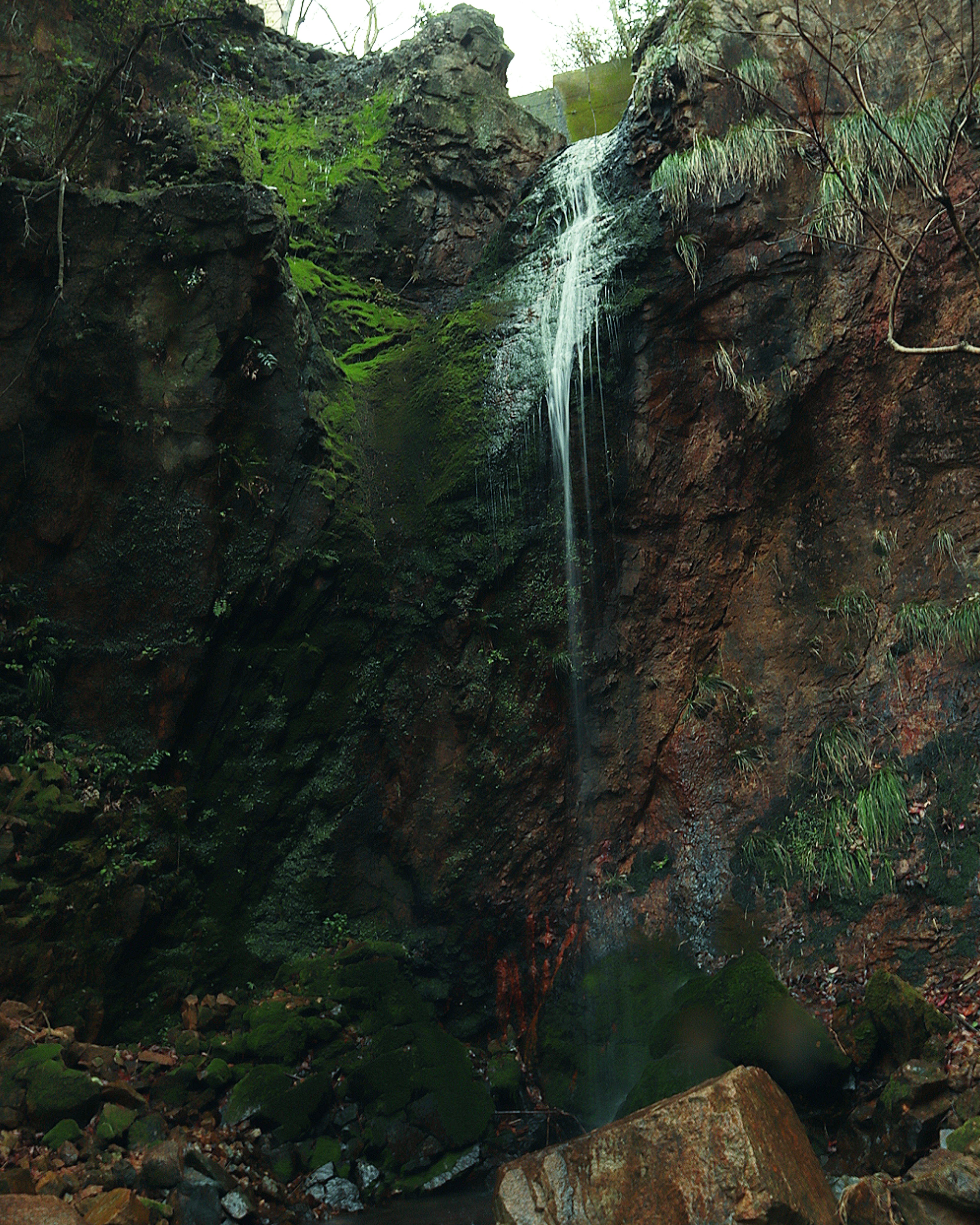 Kleiner Wasserfall, der von einer moosbedeckten Klippe mit umliegenden Steinen fließt