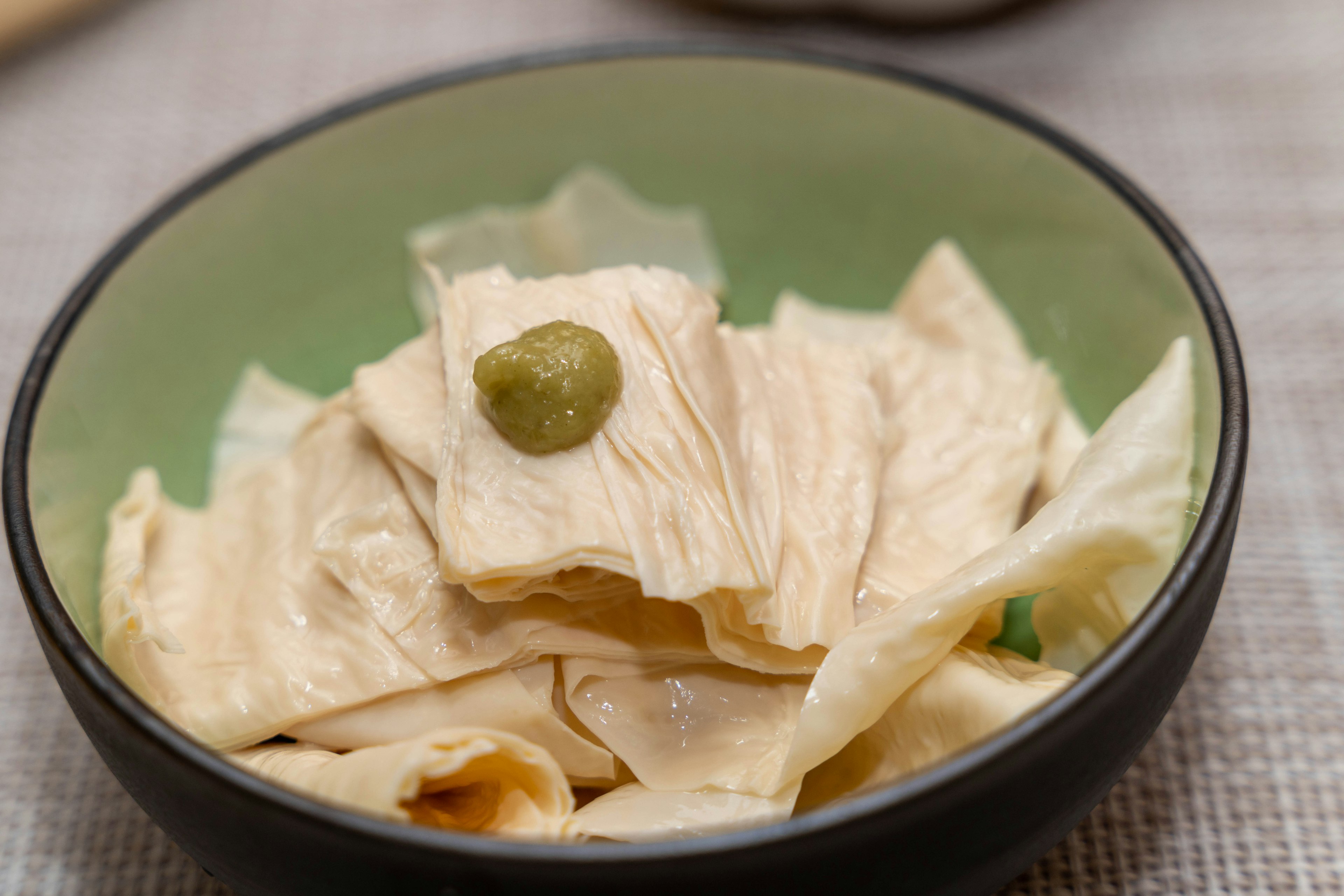 Poulet tranché fin dans un bol vert avec une touche de wasabi