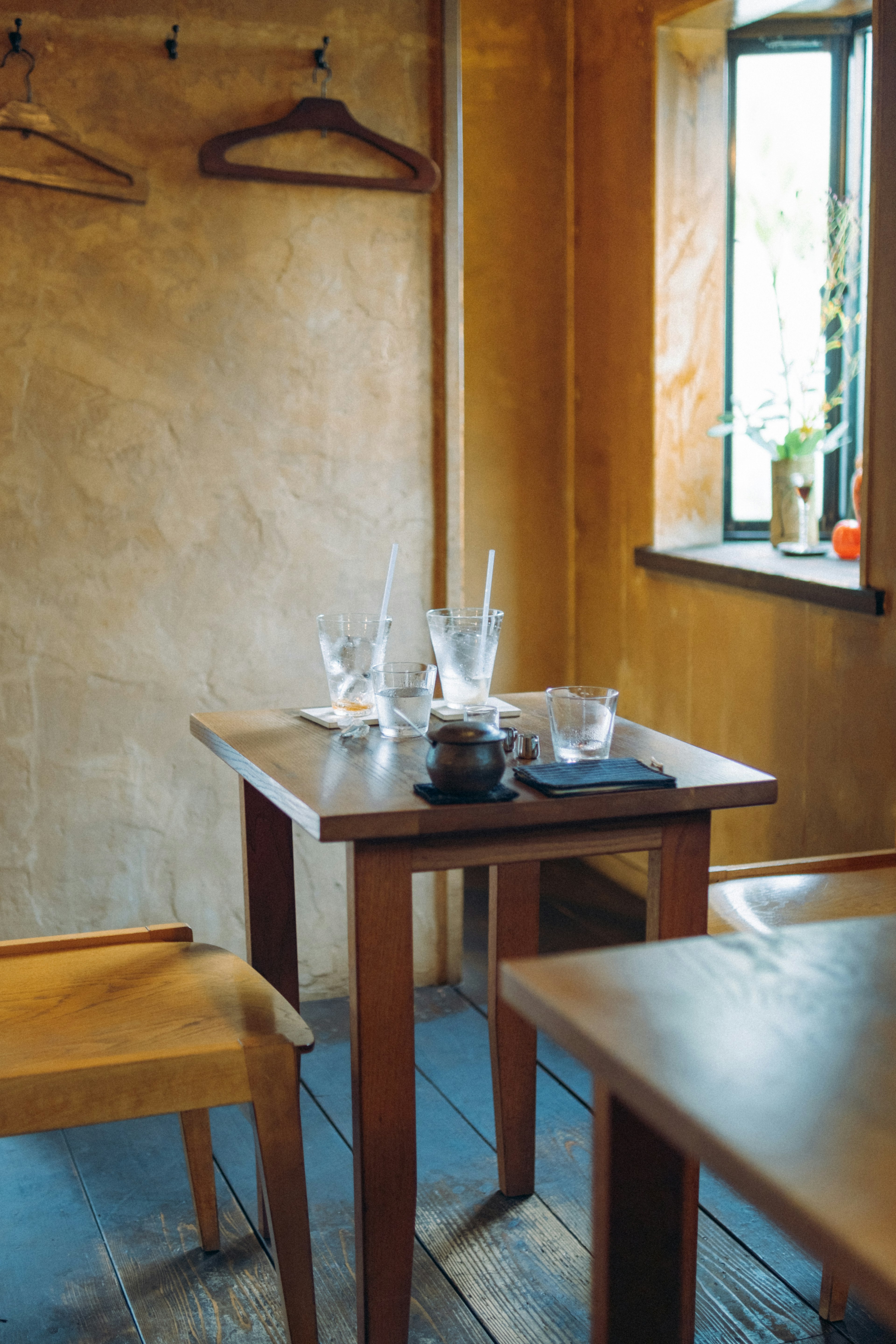 Interior de una cafetería con mesa y sillas de madera y luz natural que entra por la ventana