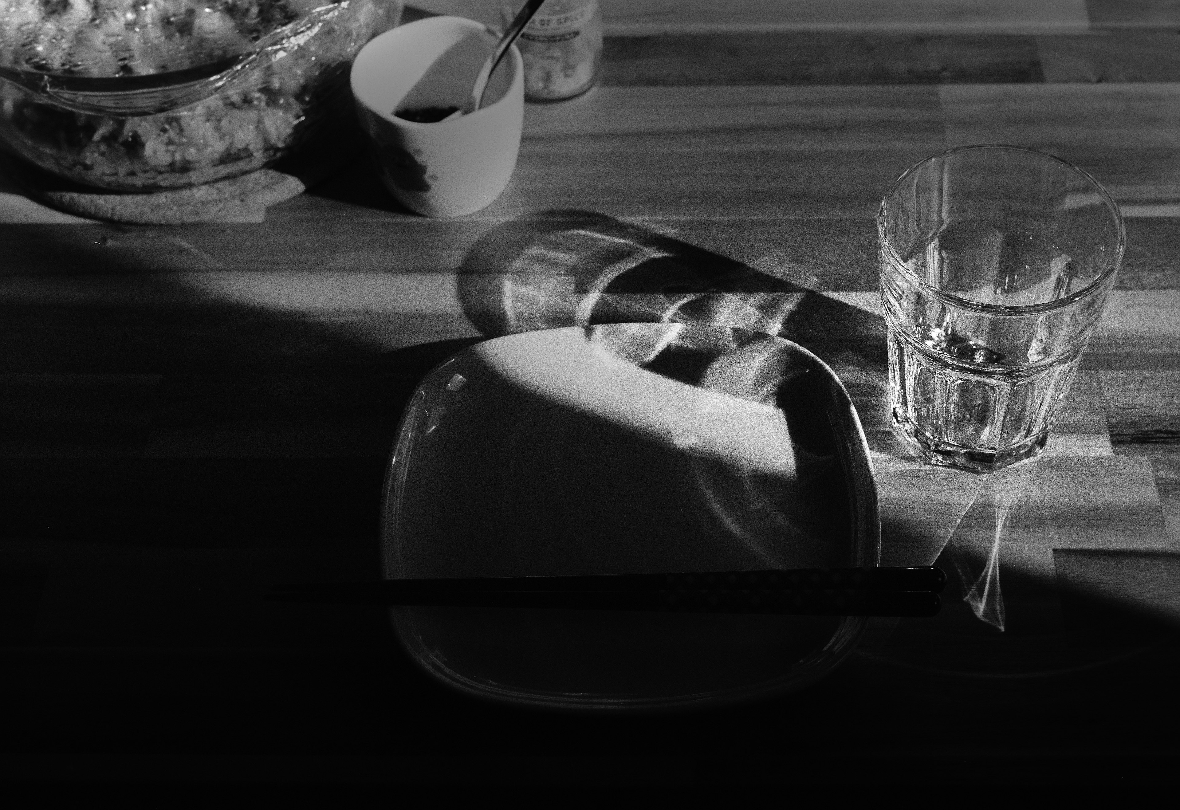 Ein schattierter Teller und ein Wasserglas auf einem Holztisch in Schwarzweiß