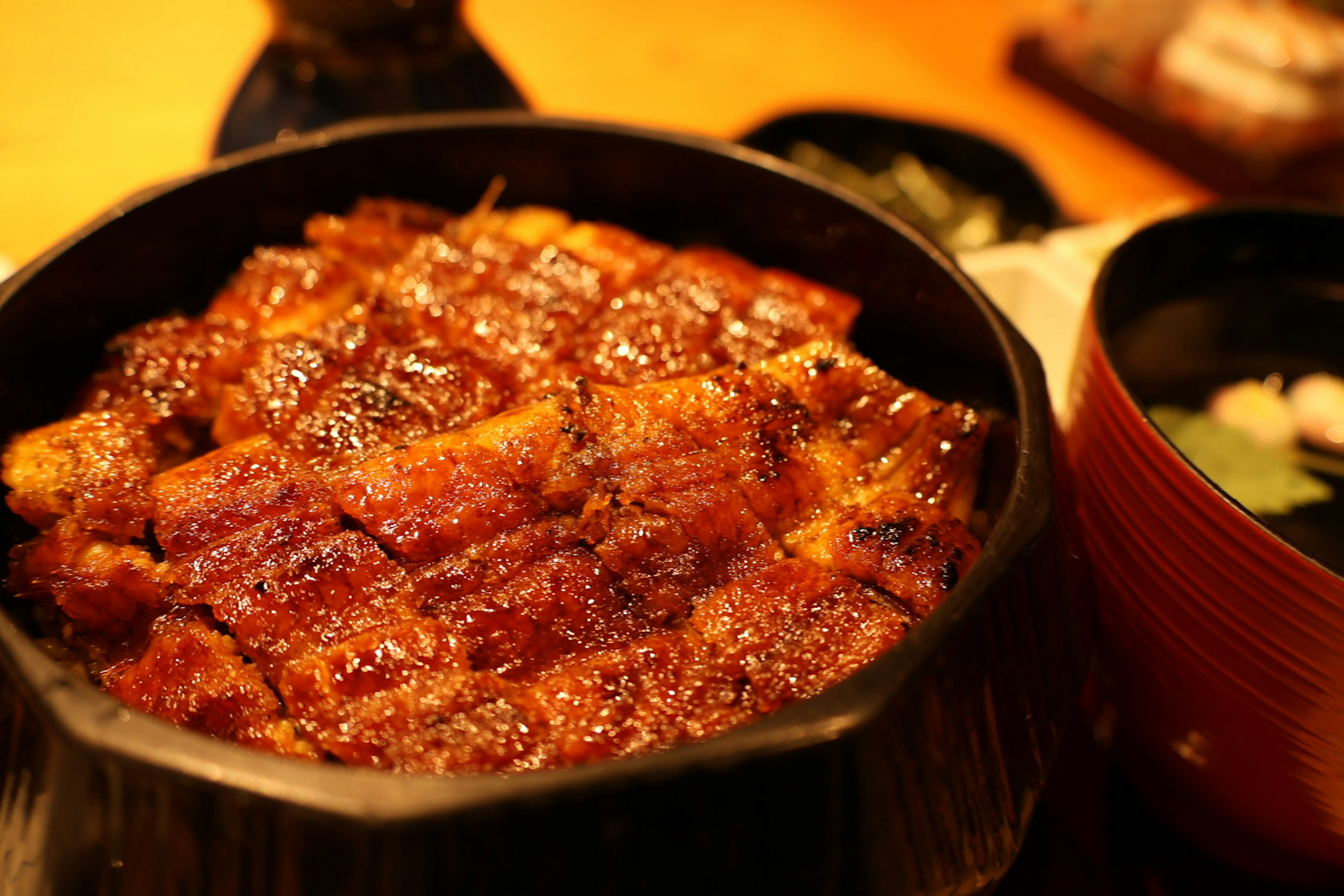 美味しそうな鰻丼が盛られた黒い器と味噌汁が写っている