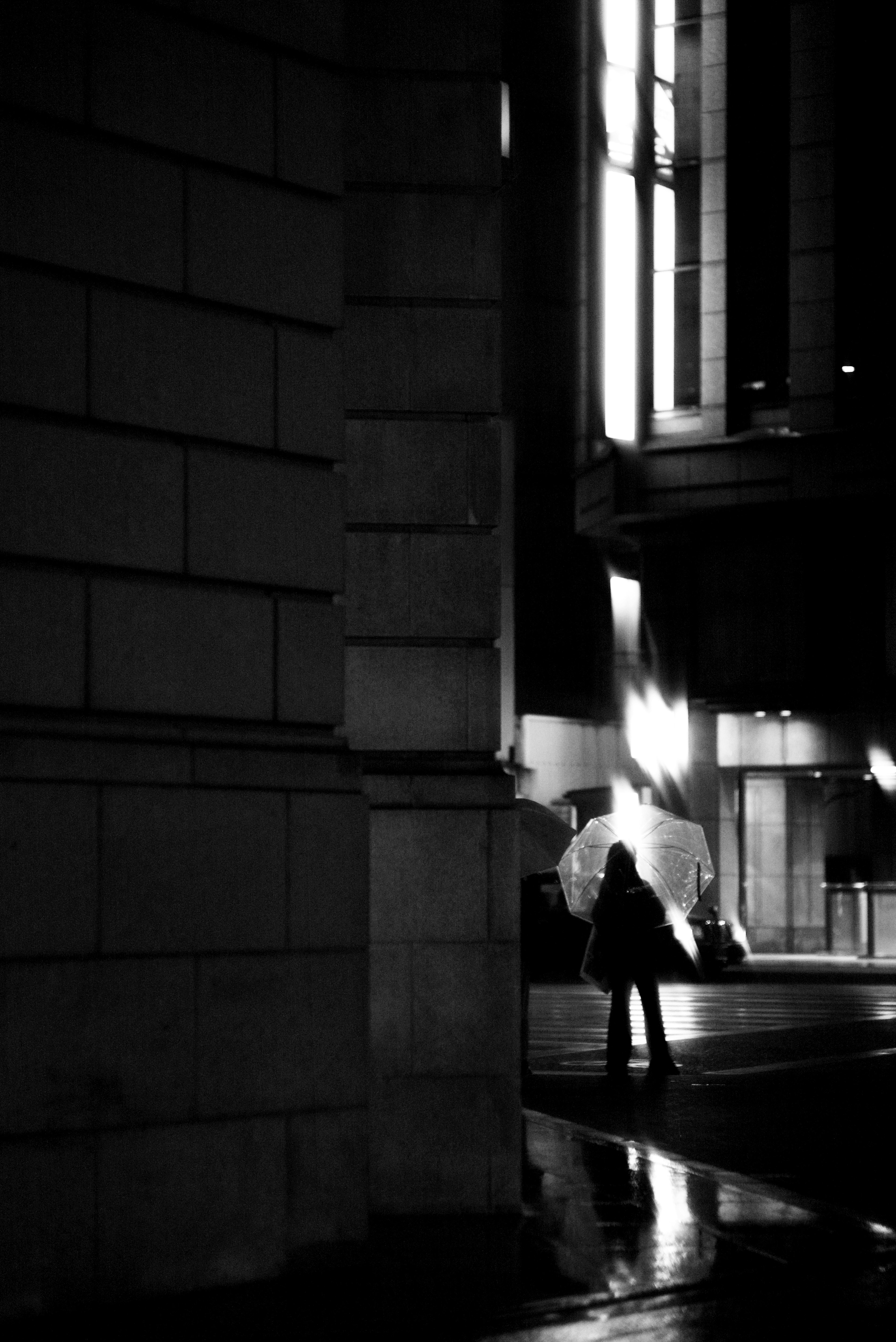 Silhouette of a person standing in a dark street near a building corner