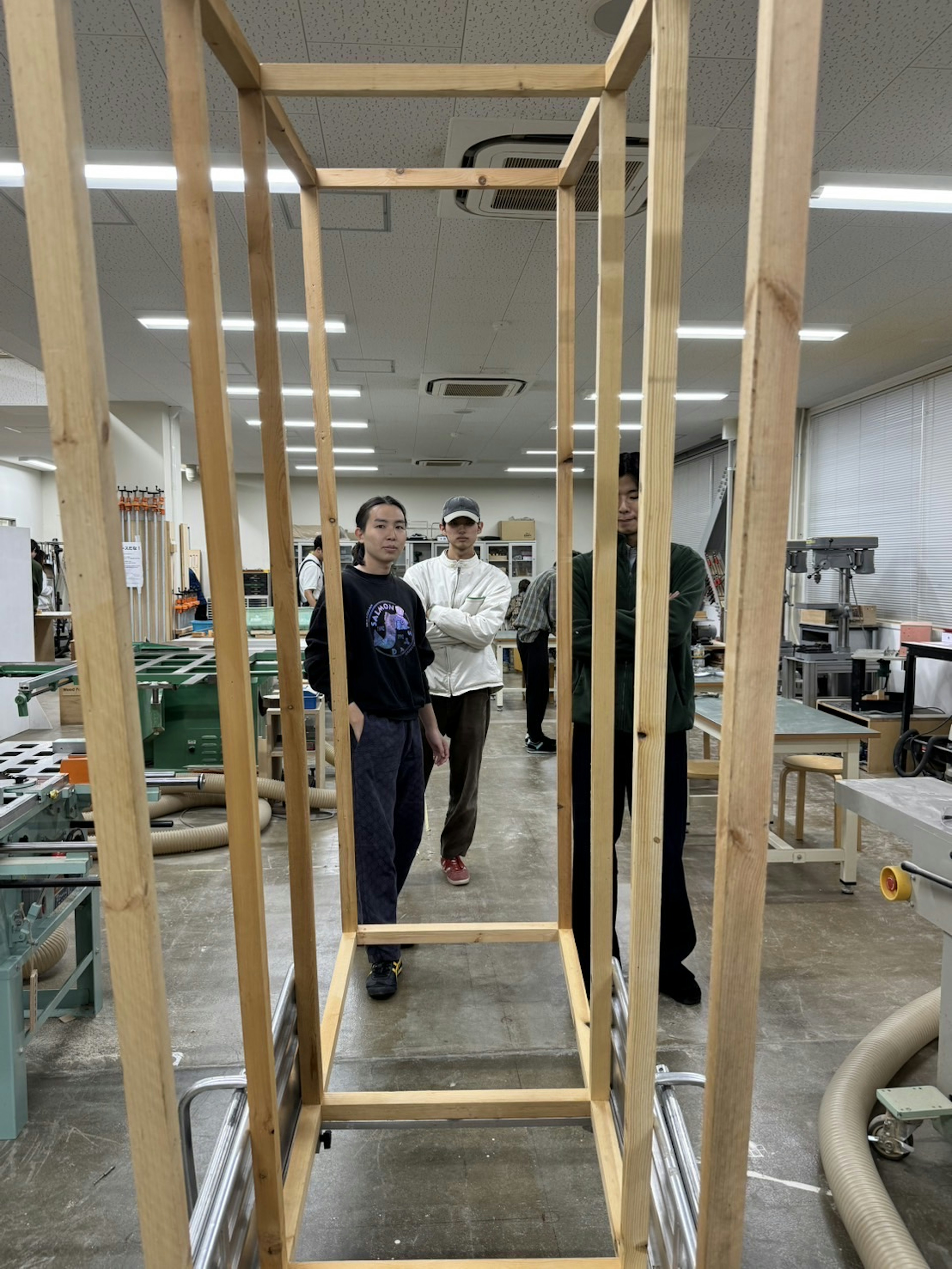 Three men standing in a workshop next to a wooden frame structure