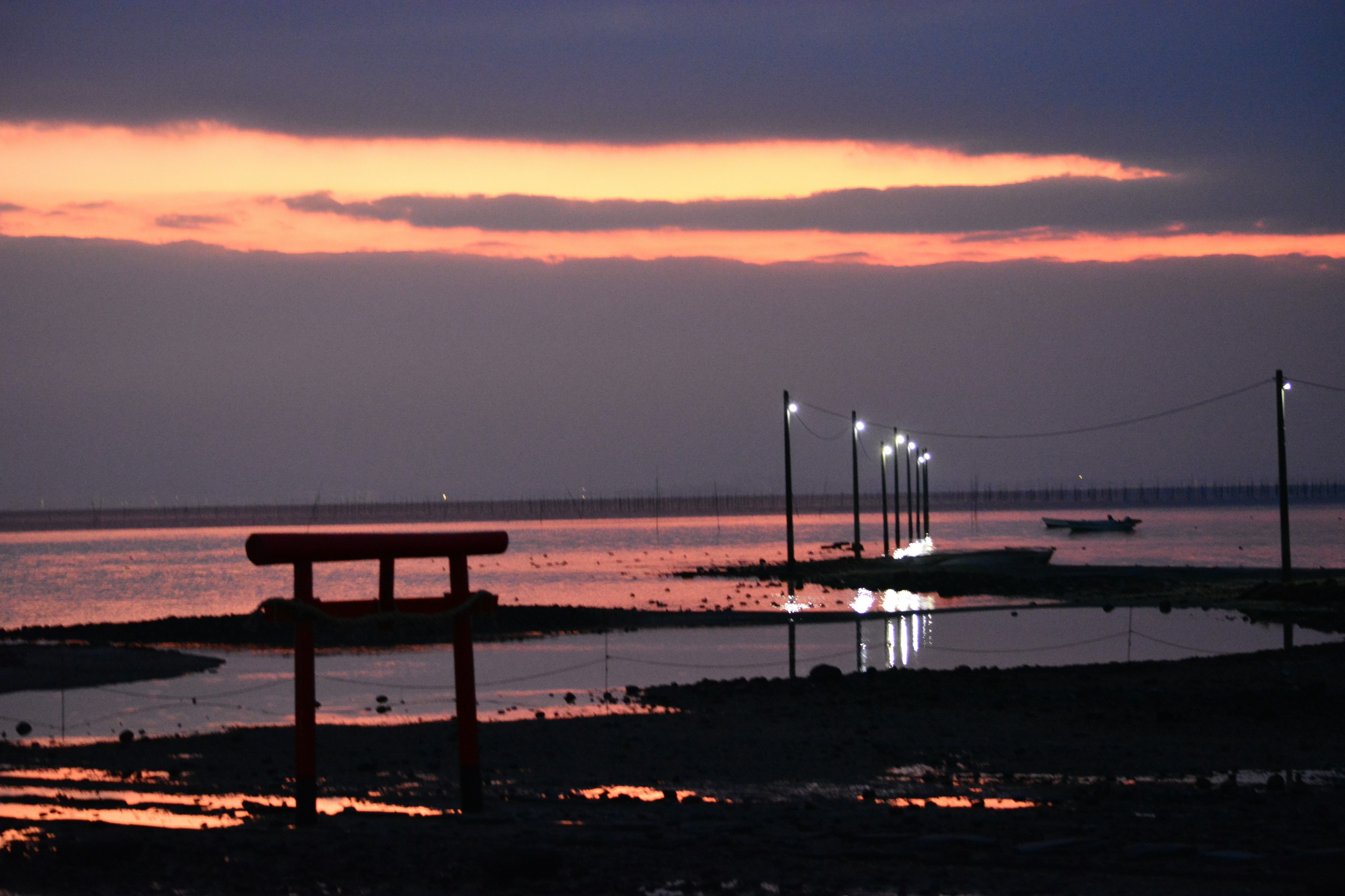 Torii am Sonnenuntergang am Ufer mit beleuchteten Lampen