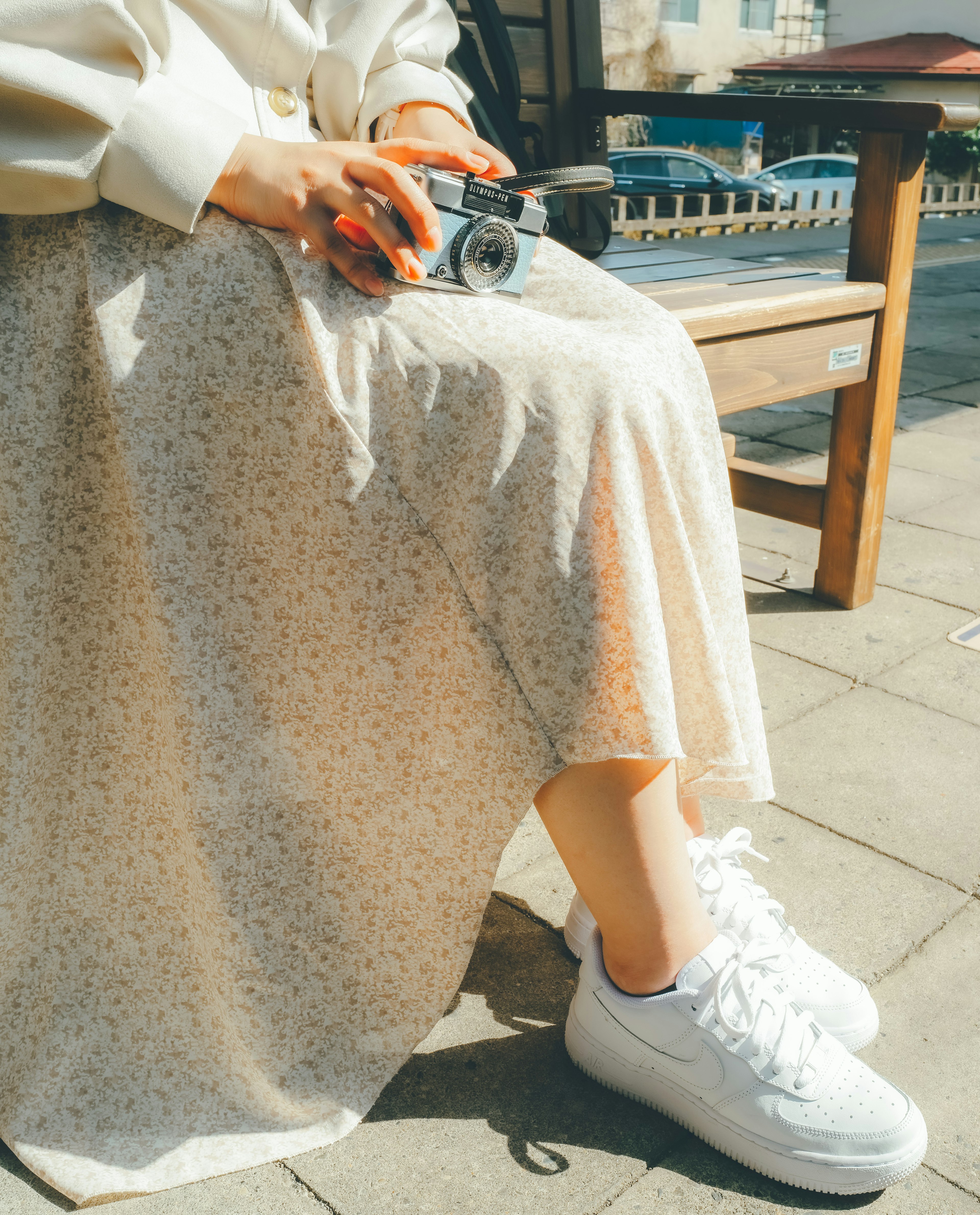 Kaki wanita dengan sneakers putih dan rok floral dalam suasana luar ruangan