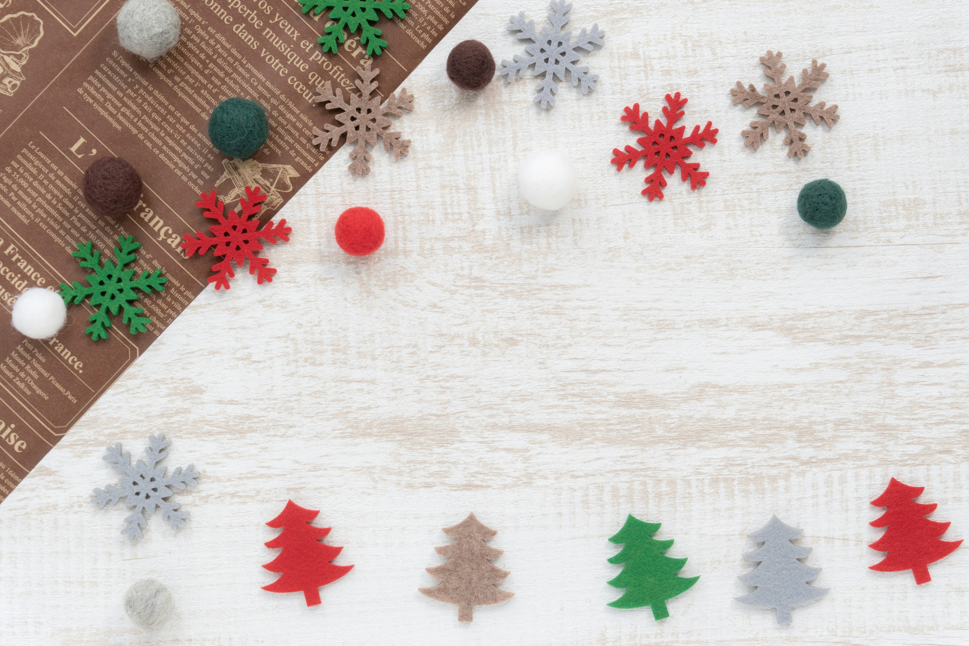 Décorations de Noël en feutre coloré comprenant des arbres et des flocons de neige rouges, verts, blancs et marron disposés sur une surface en bois