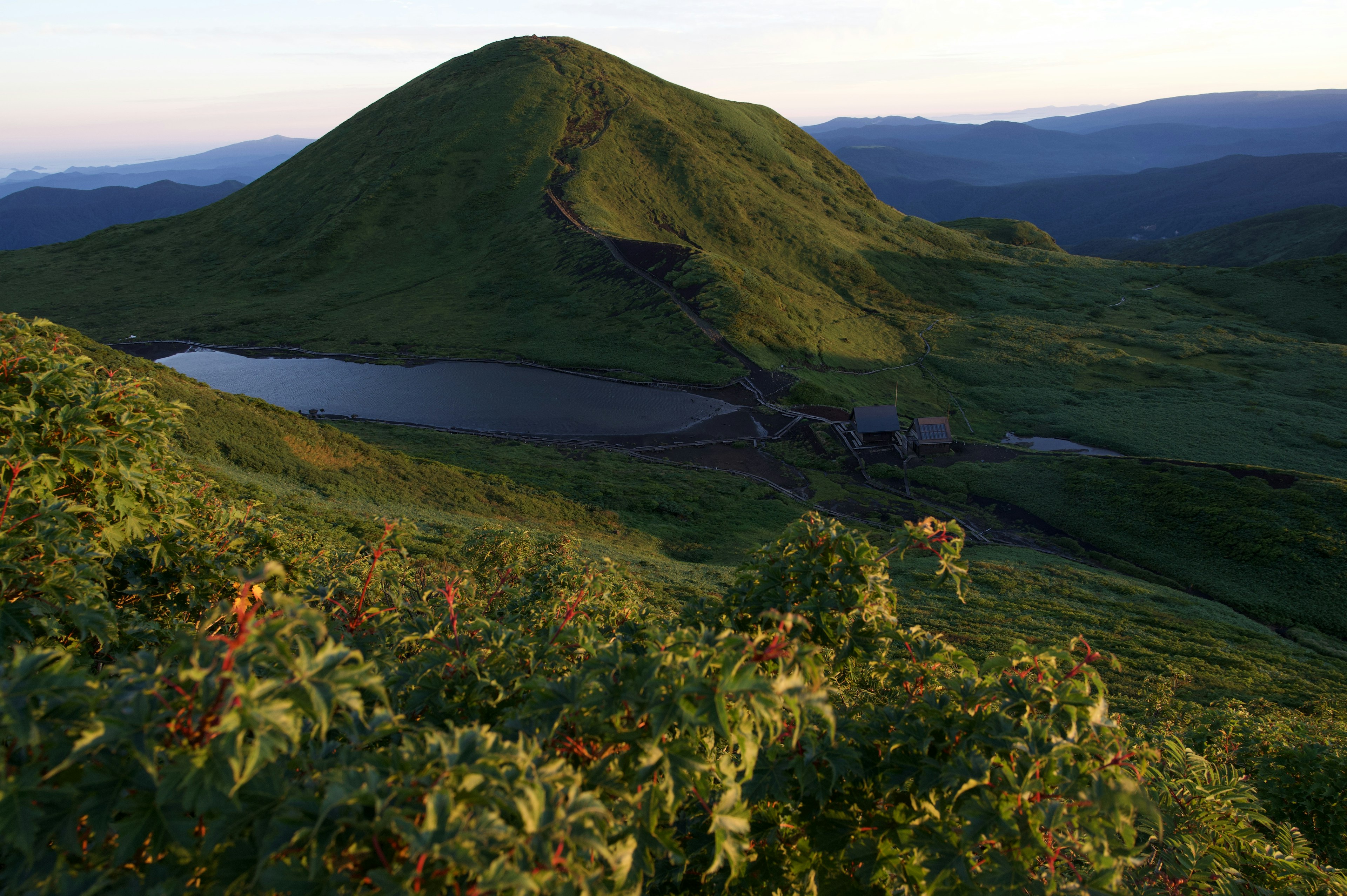 Bukit hijau subur dengan danau tenang di latar depan