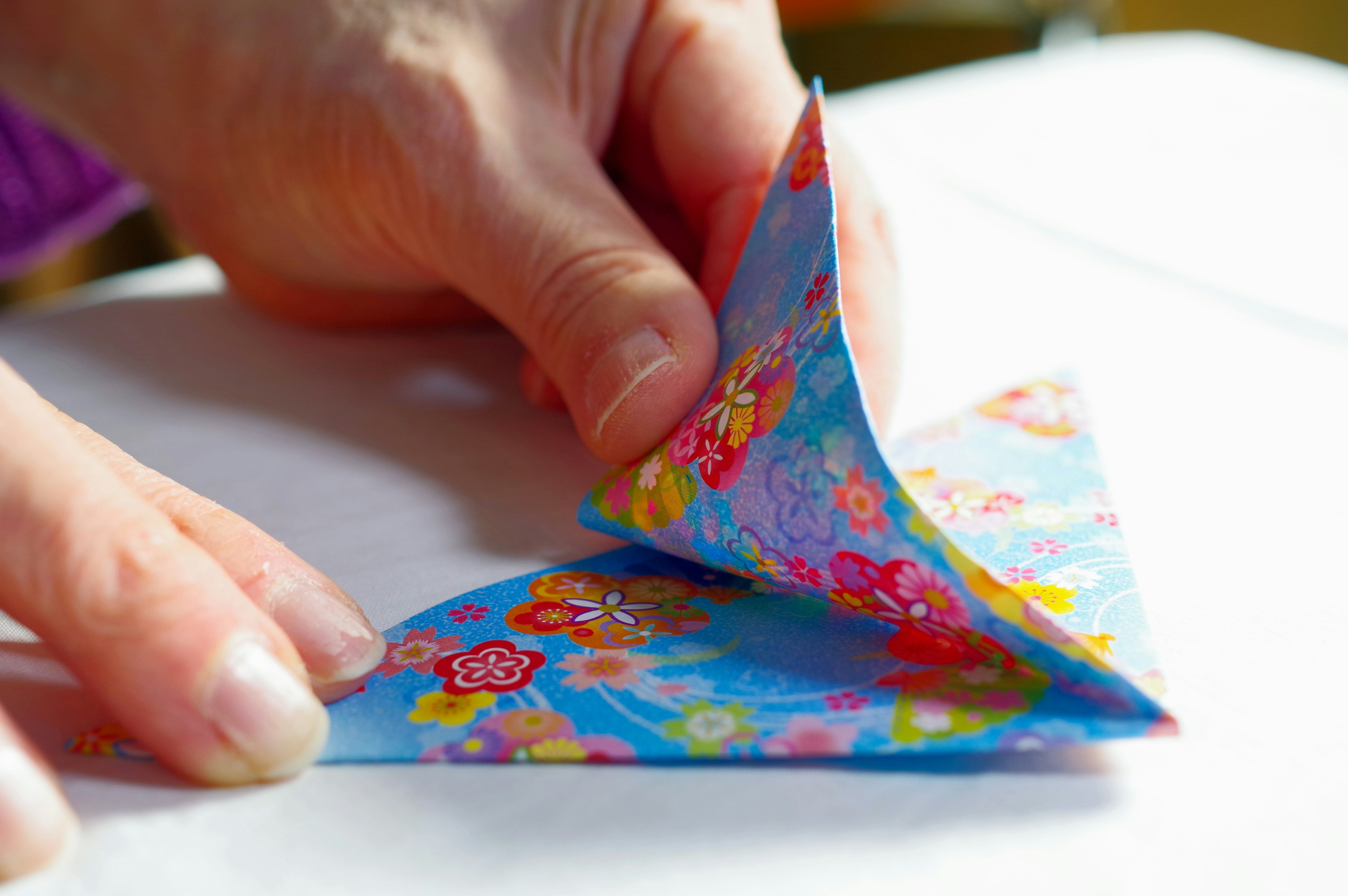 A person folding colorful floral patterned origami paper