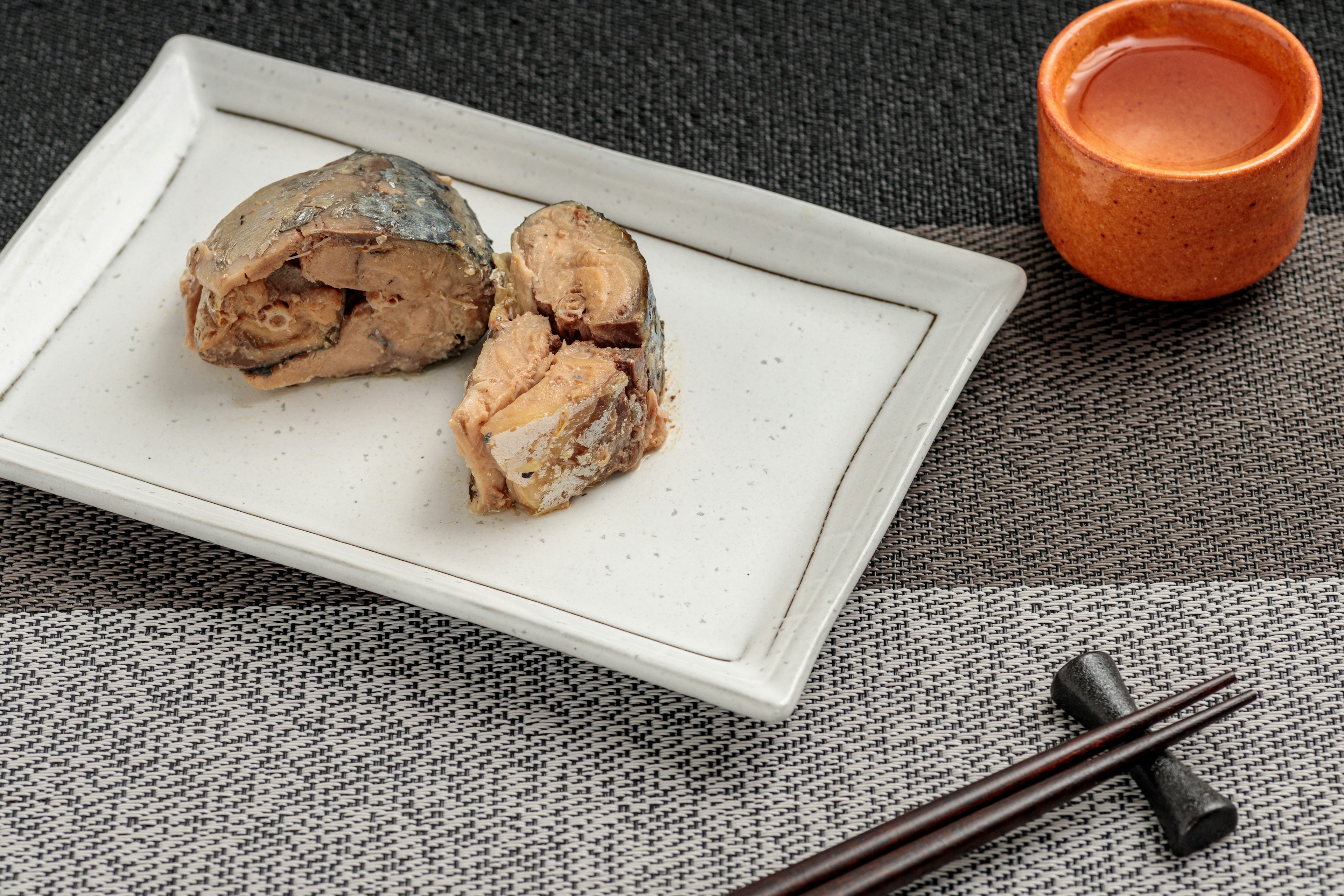 Tranches de poisson grillé sur une assiette blanche avec une petite tasse orange de boisson