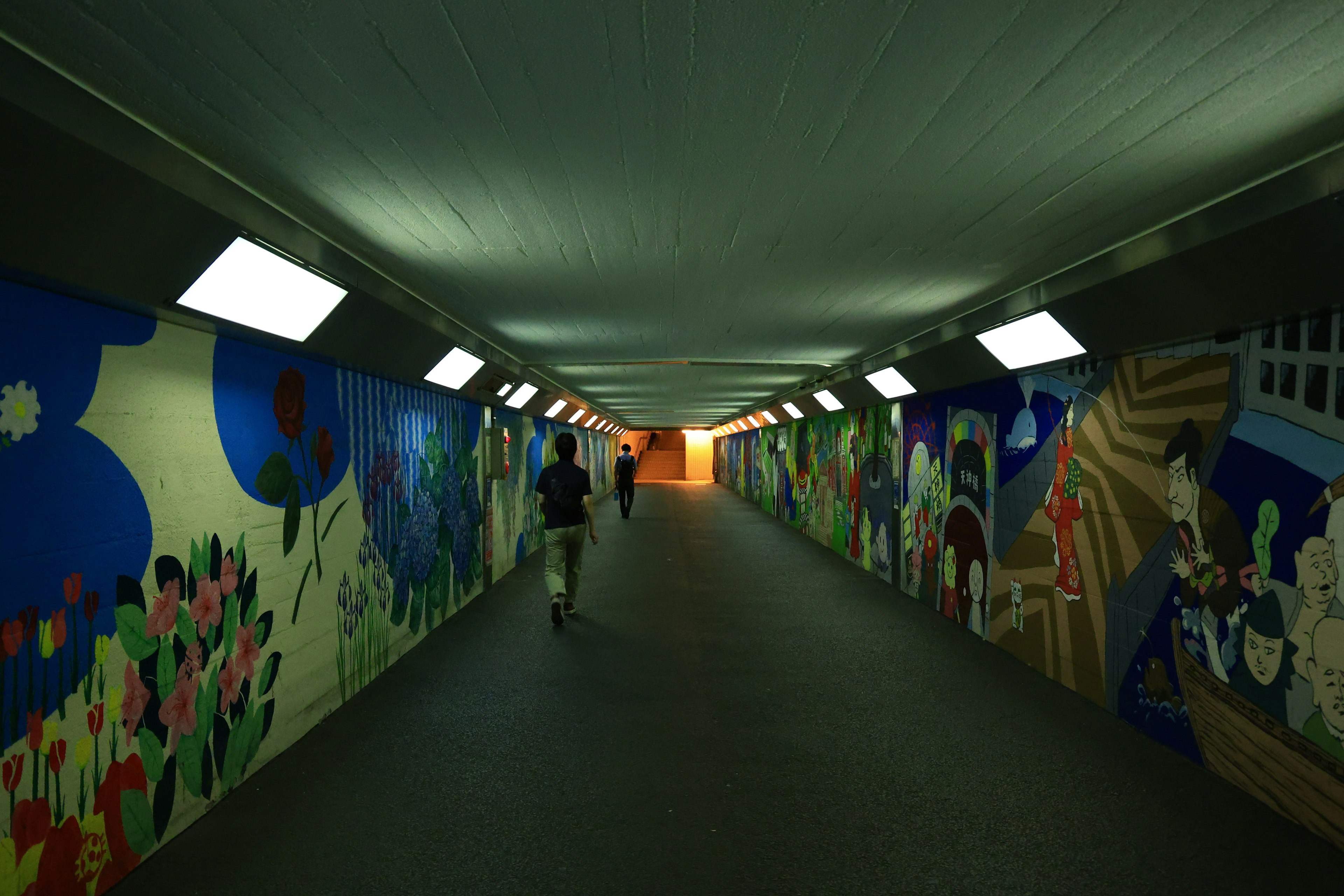 Colorful murals on the walls of a bright tunnel with a person walking