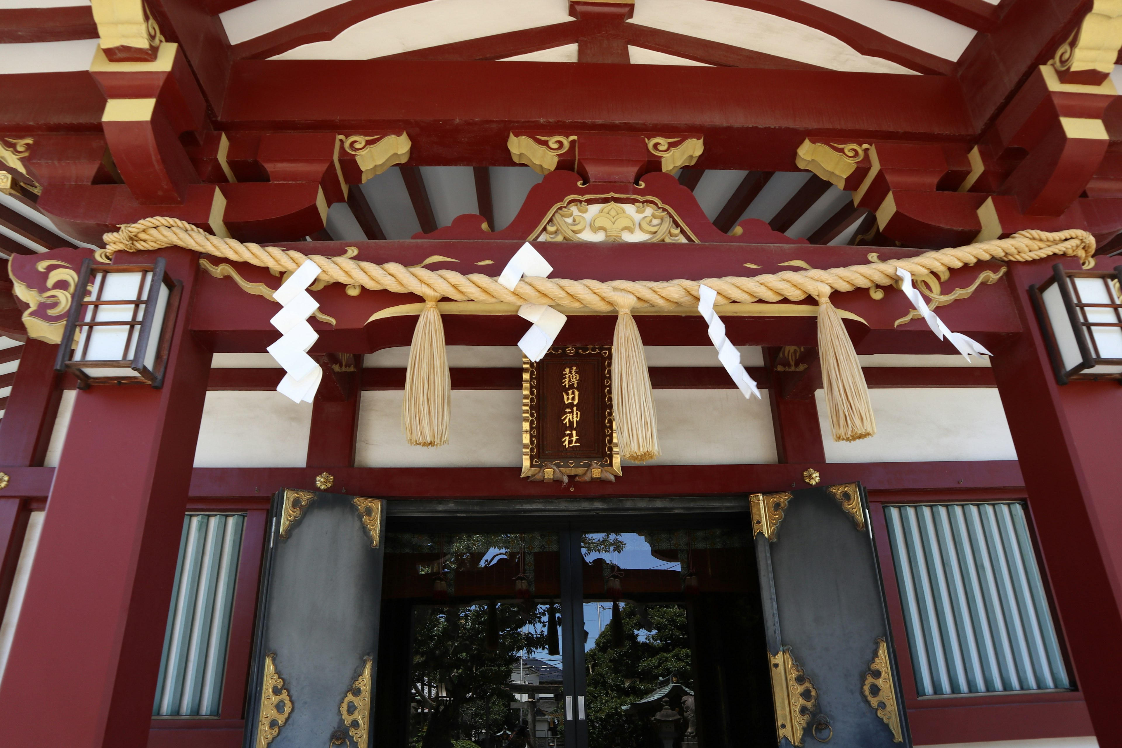 Entrance of a red-roofed shrine featuring decorative lanterns and rope