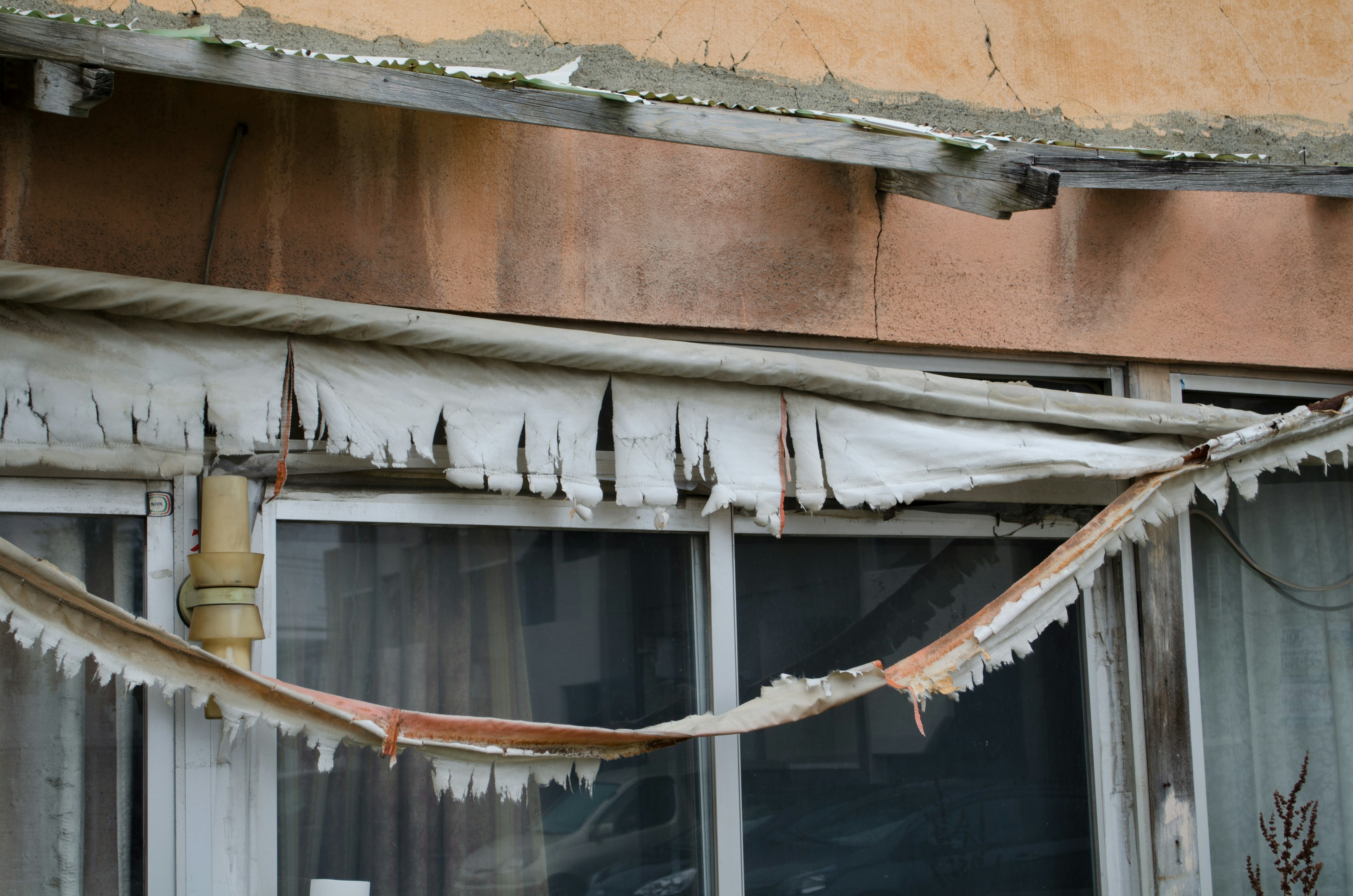 Esterno di un edificio in deterioramento con materiale di copertura sfilacciato che pende sopra una finestra