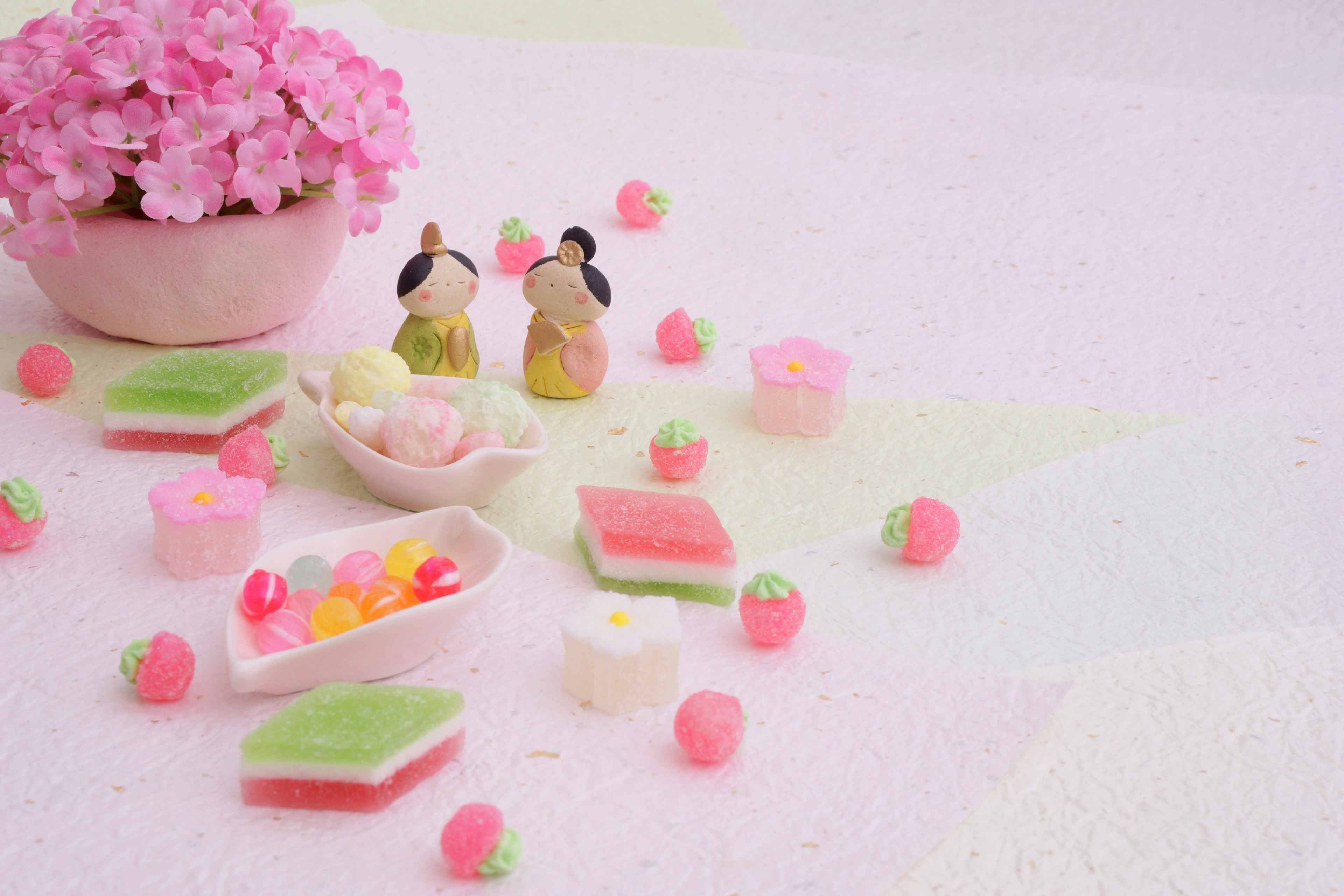 Une table avec un pot de fleurs roses et des sucreries japonaises colorées avec deux figurines mignonnes à proximité