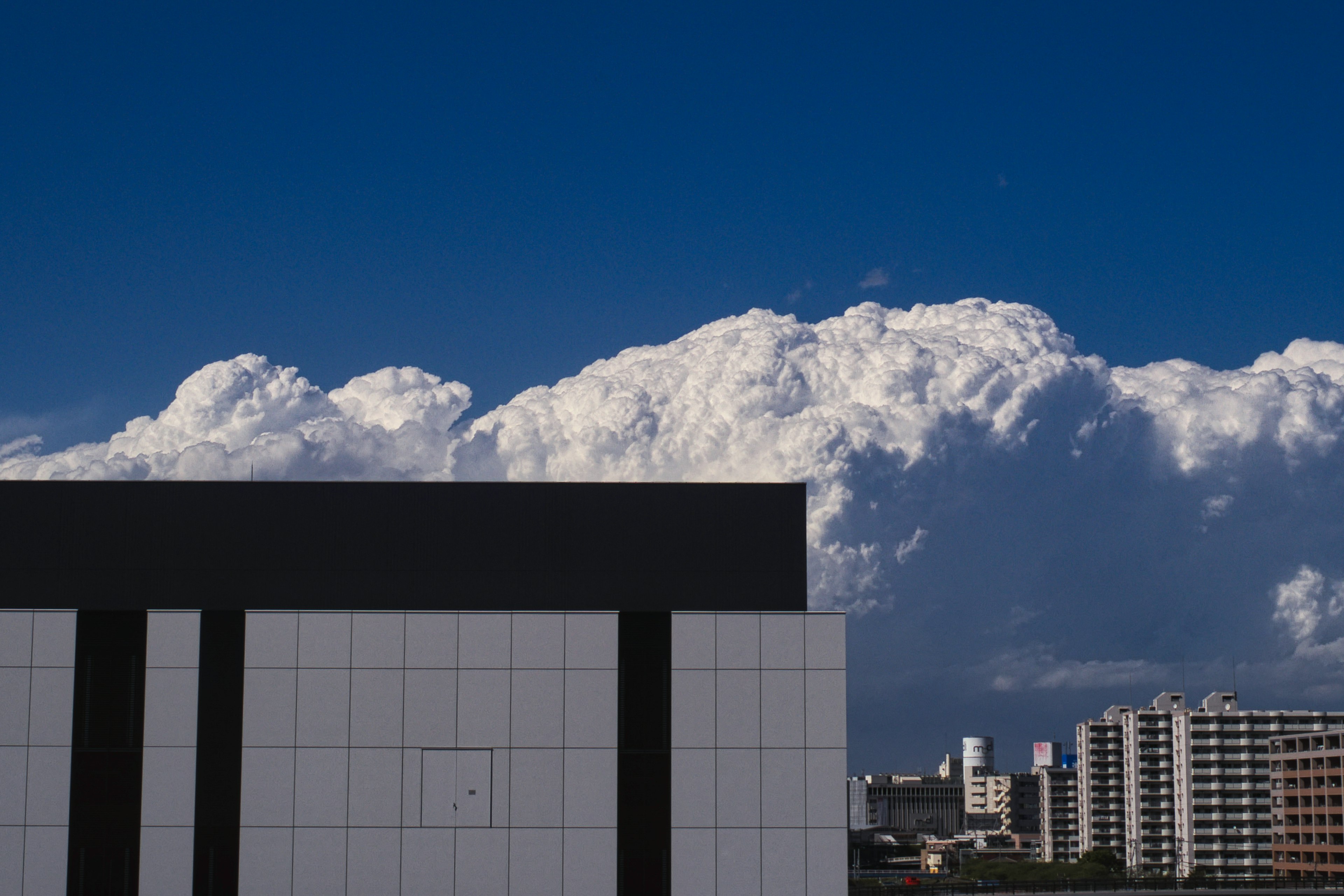 青い空と白い雲が広がる背景に、黒い縦線のある白い建物が映える風景