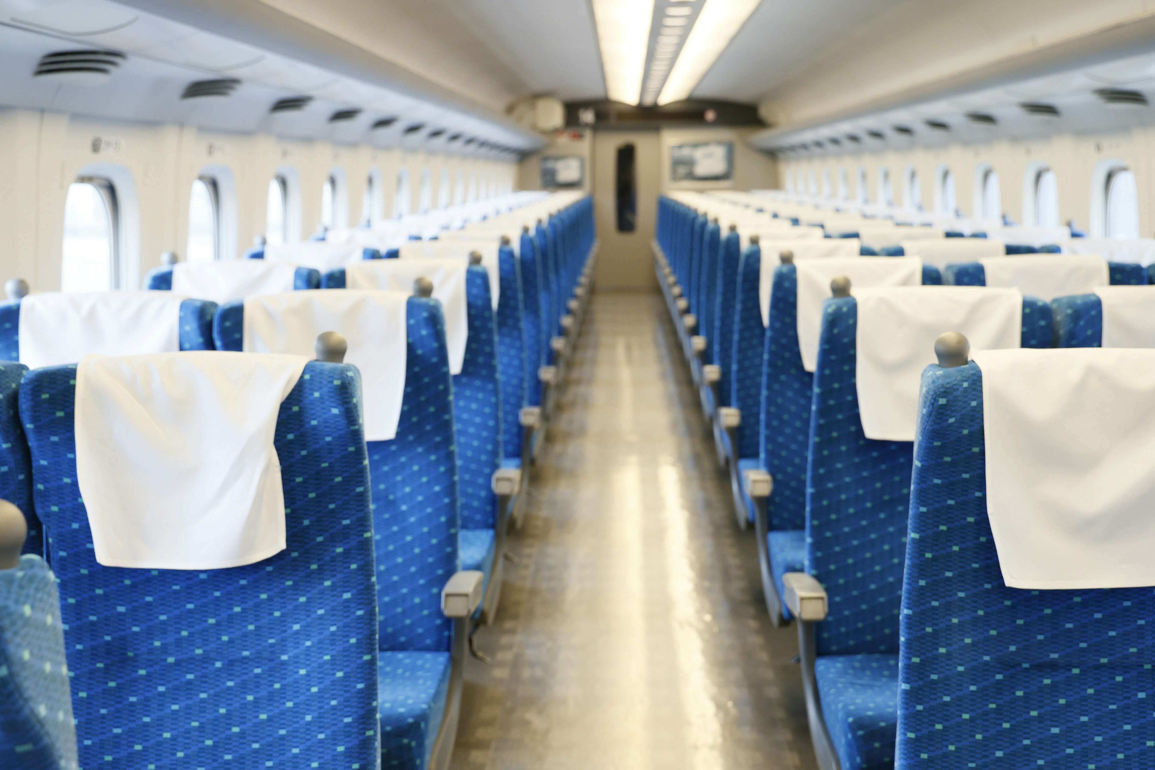 Interior de un tren Shinkansen con asientos azules y toallas blancas