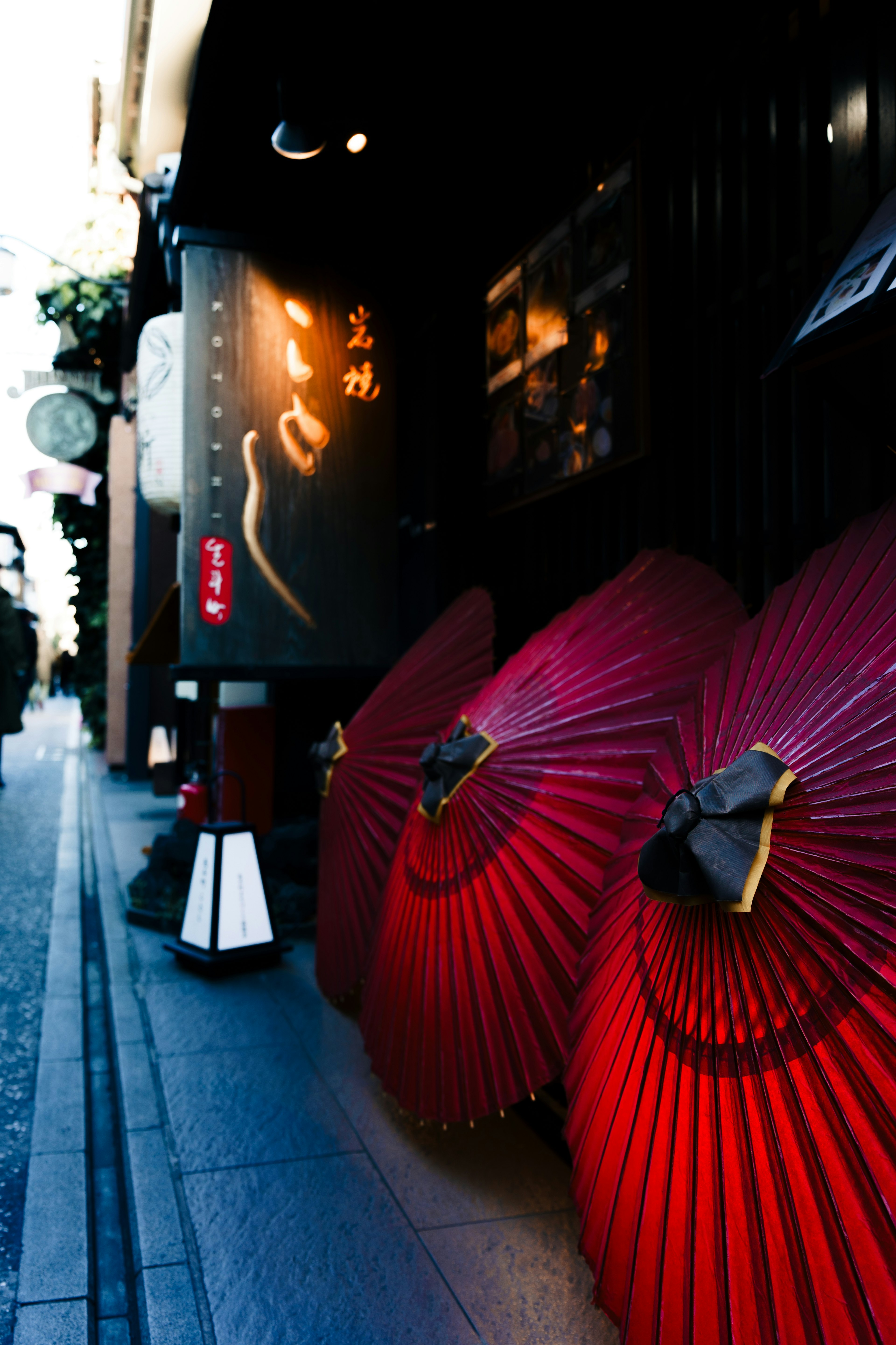 Narrow street scene with red umbrellas and a black storefront