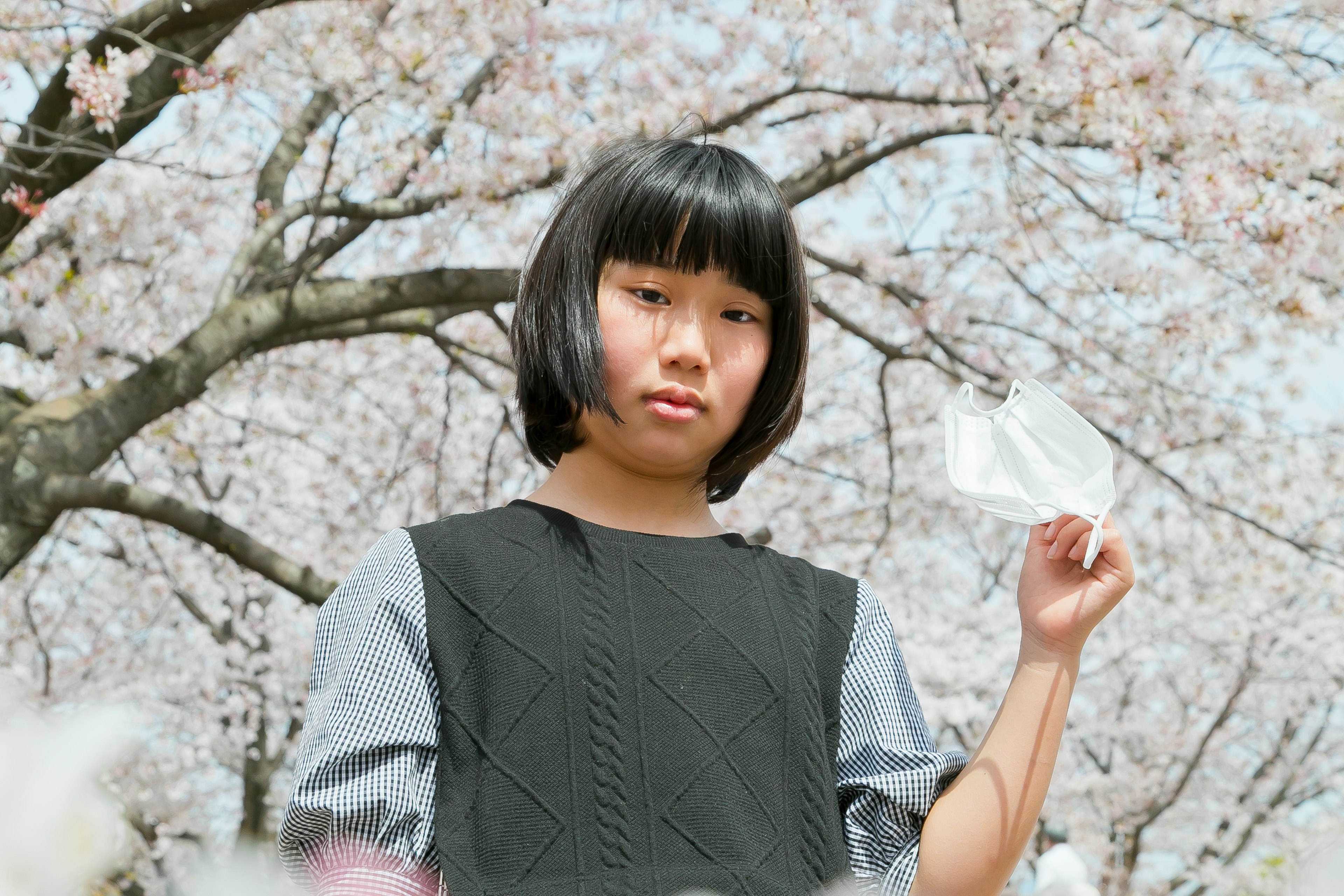 A girl standing under a cherry blossom tree holding a white piece of paper