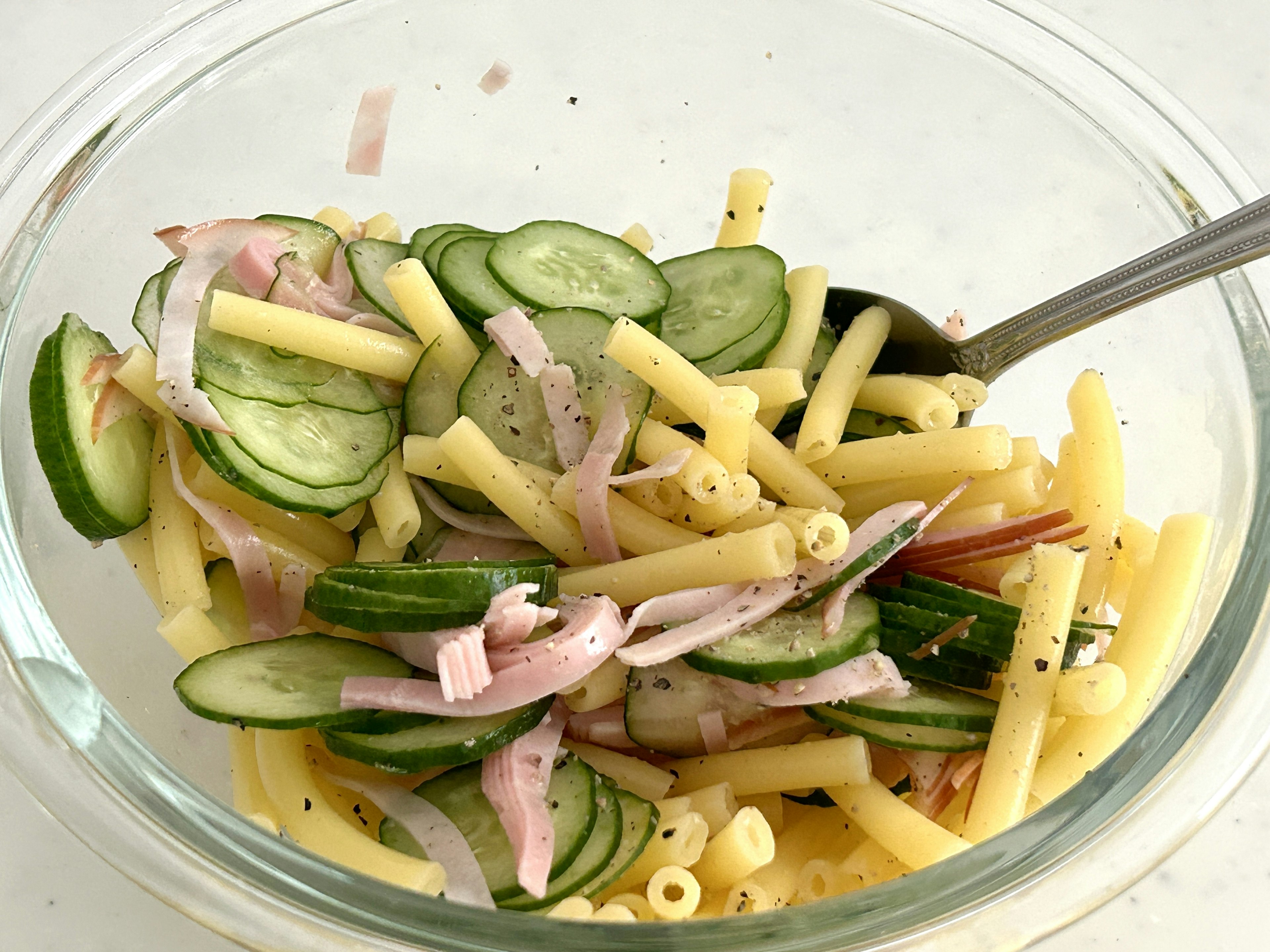 A bowl of pasta salad with cucumber and sliced ham