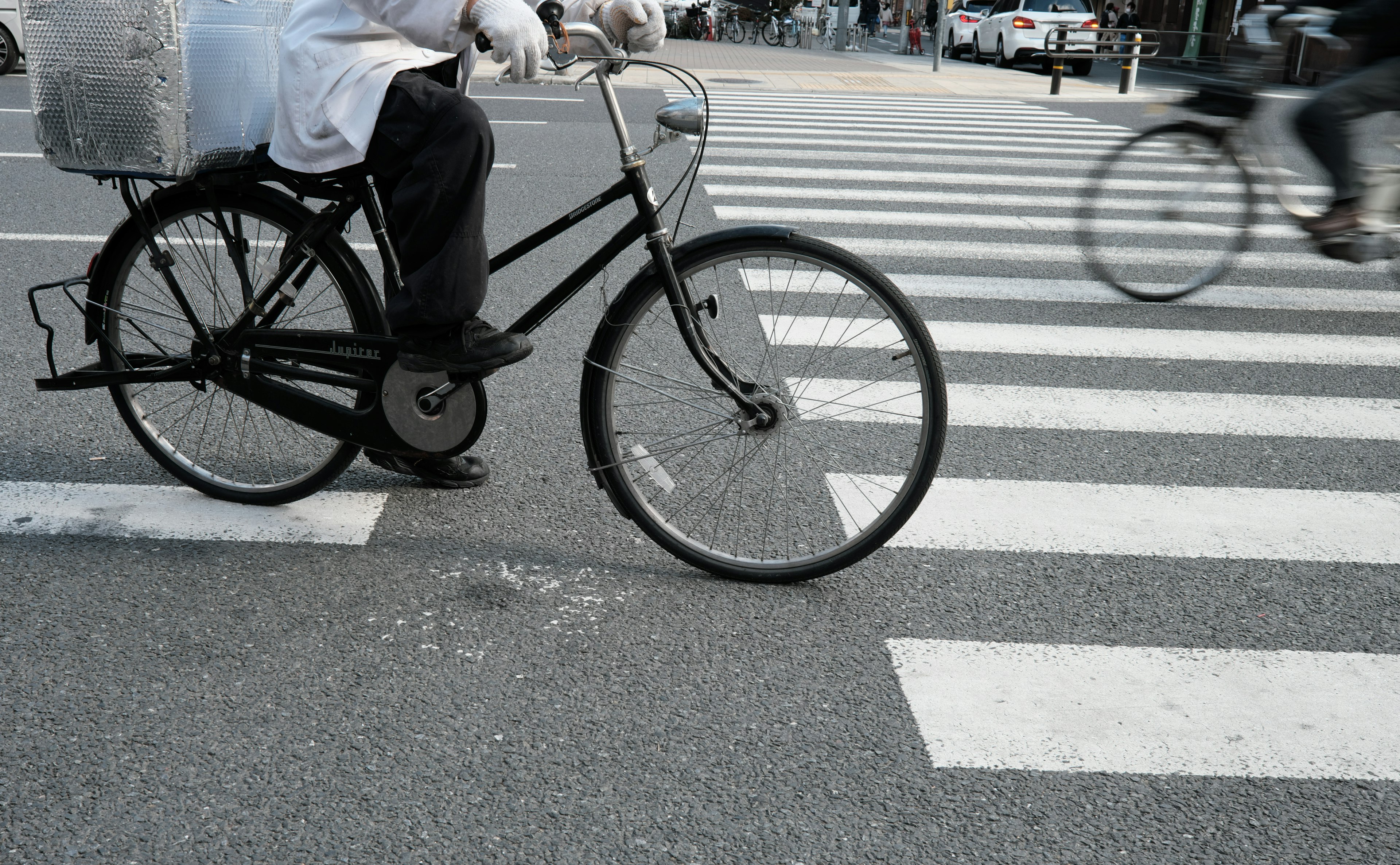 Seorang pengantar makanan mengendarai sepeda melintasi zebra cross