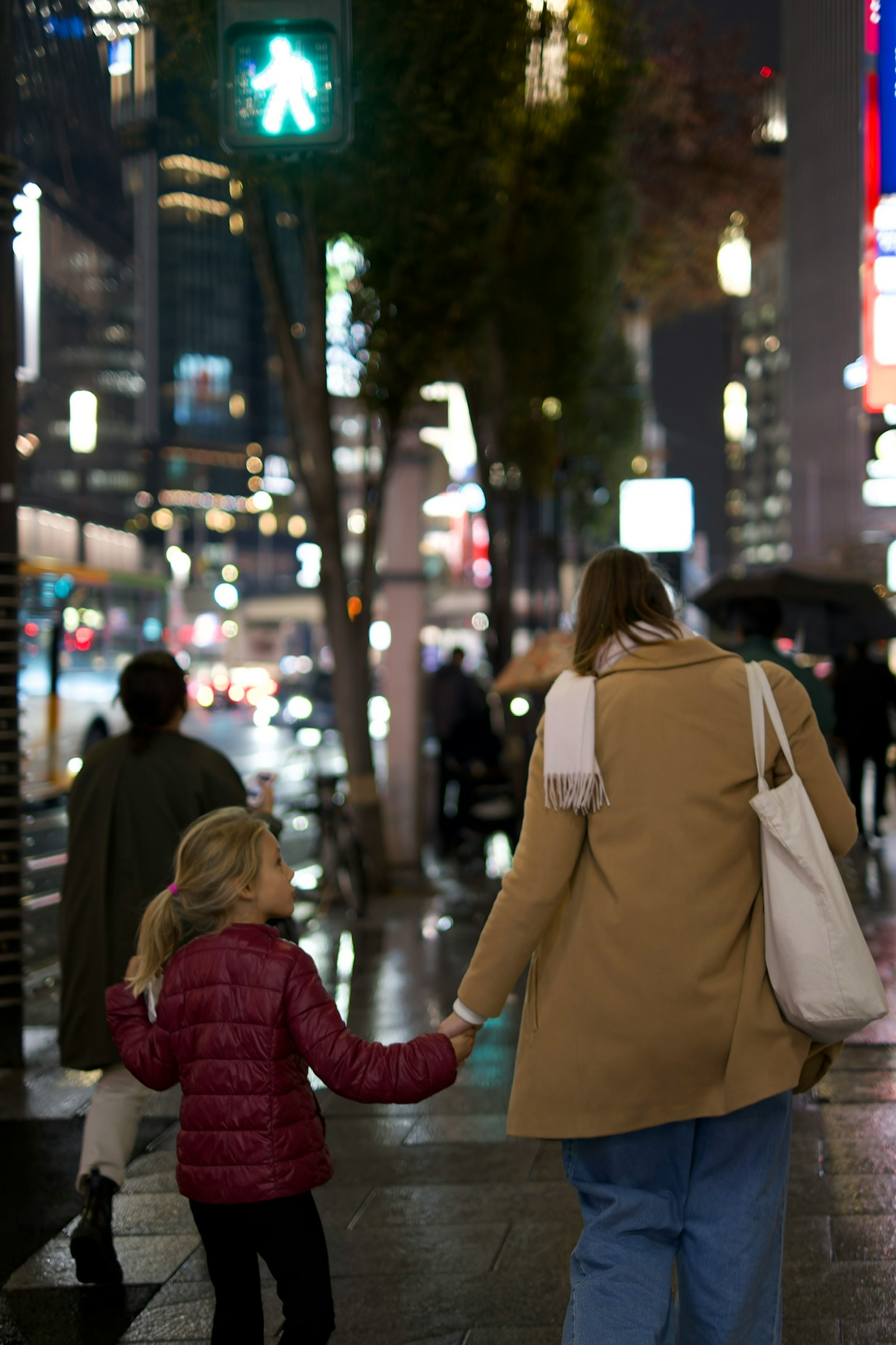 Adult and child walking on a city street at night bright signals and neon lights in the background