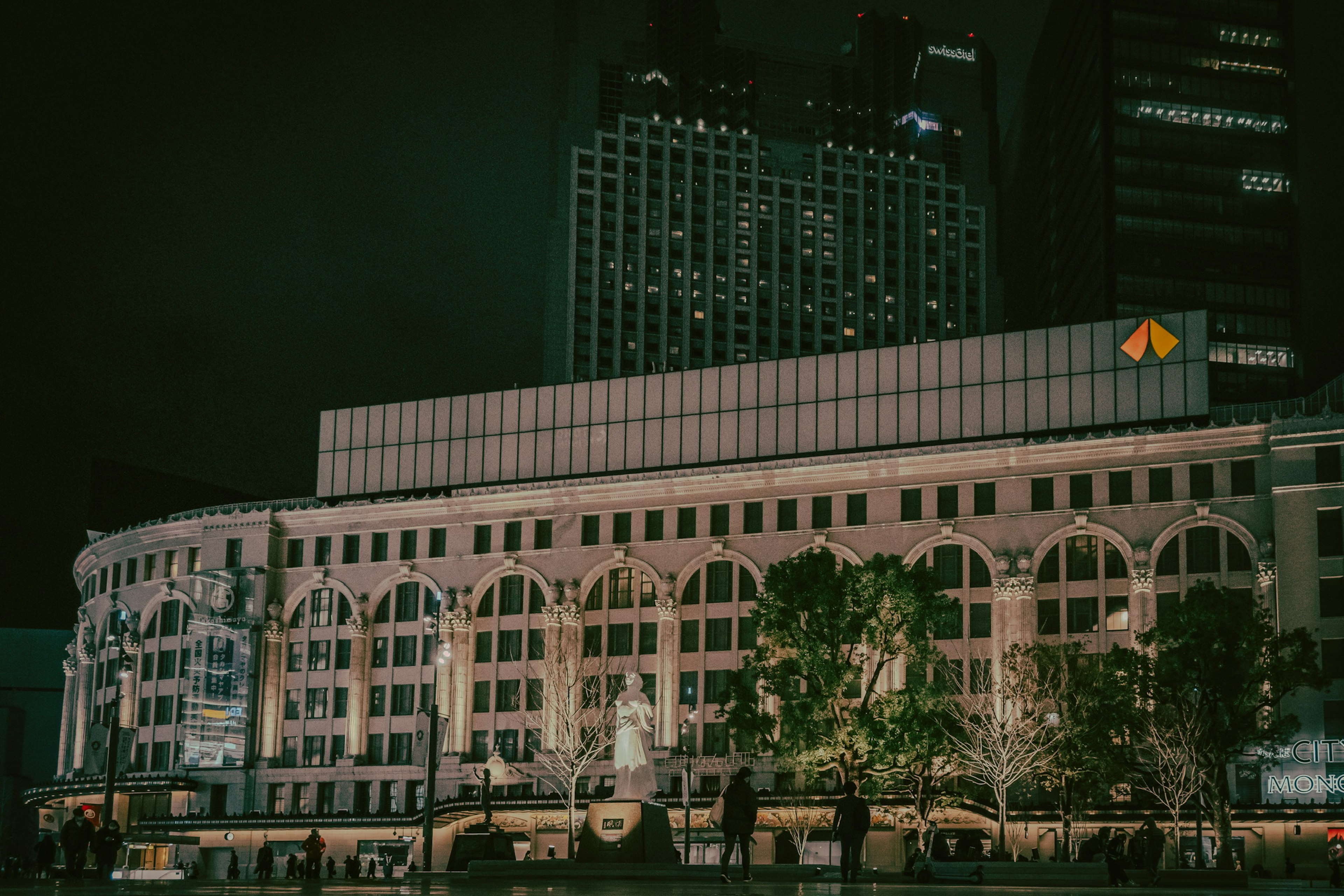 Large building illuminated at night surrounded by green trees