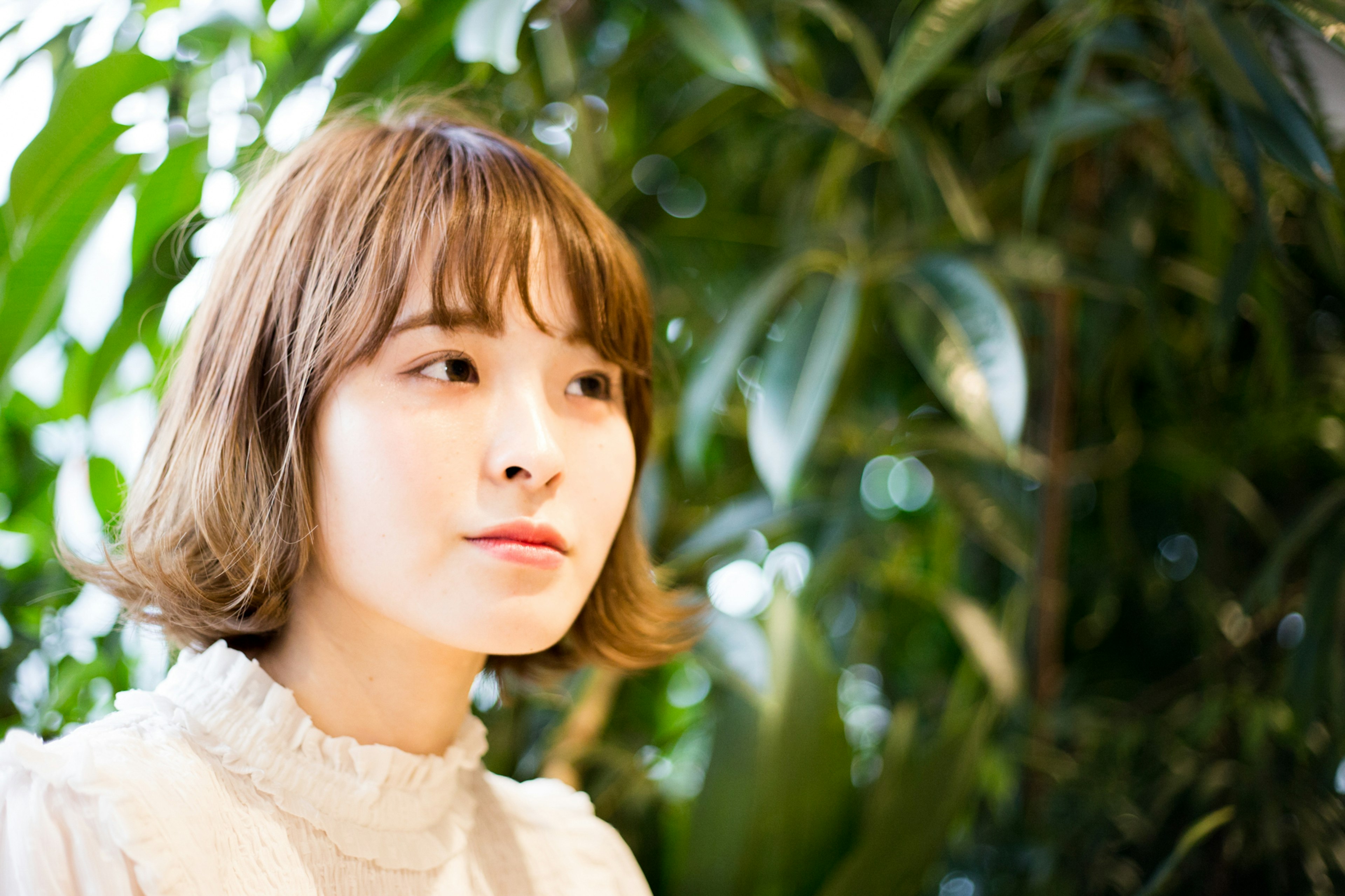 Portrait of a young woman in front of green plants she has short hair and is wearing a white outfit